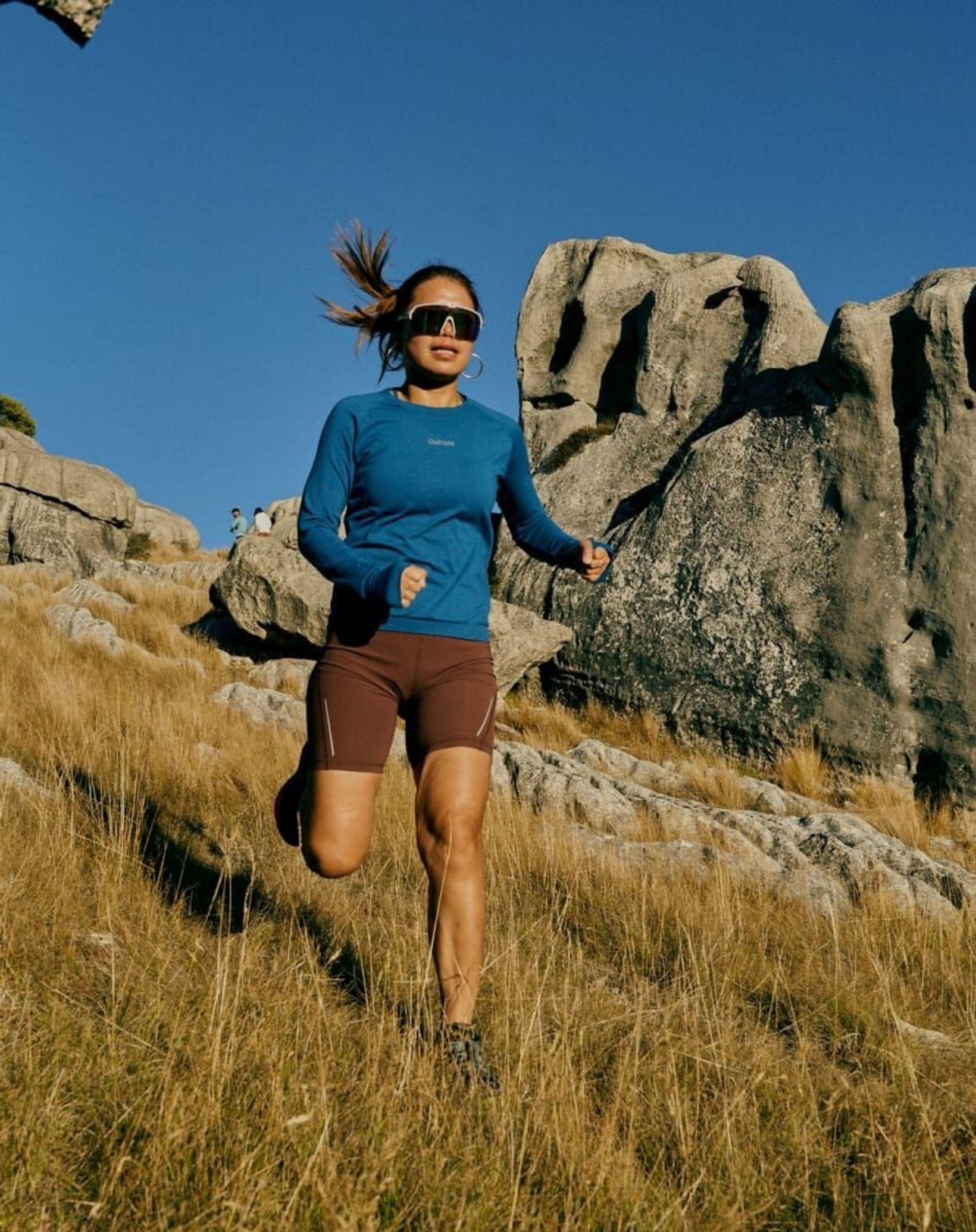 Runner in a blue top running down a grassy slope beside limestone rocks