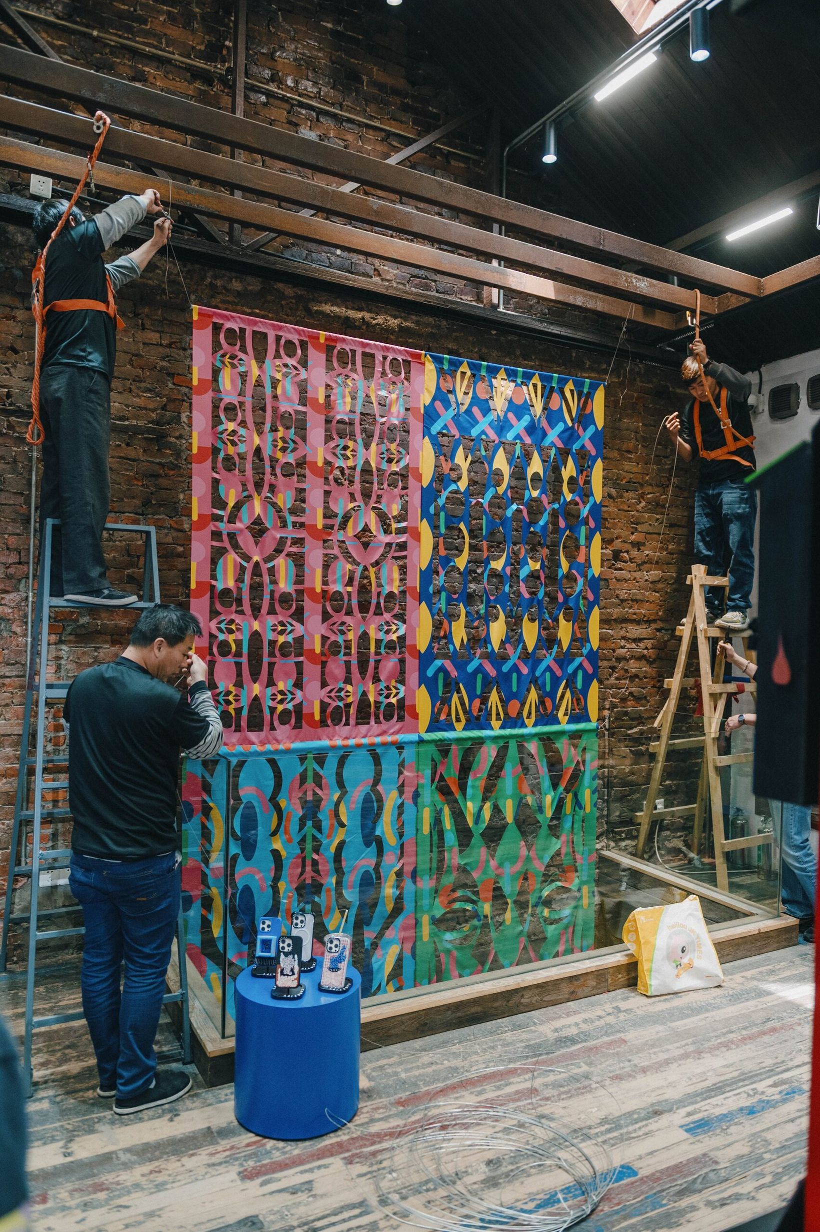 Artists on ladders painting a patterned mural on a brick wall