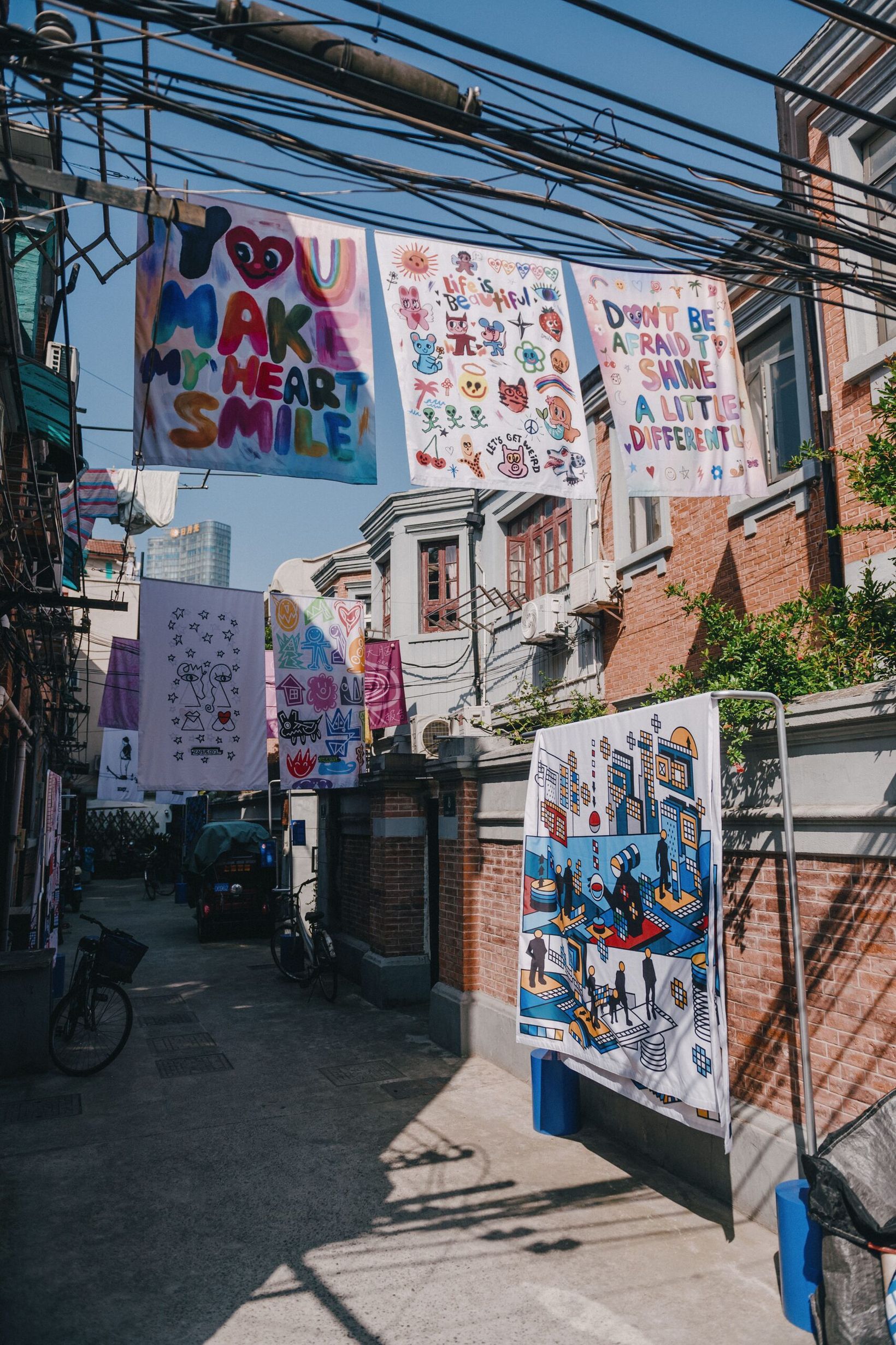 Colourful artwork sheets strung on wires above a narrow Shanghai alley