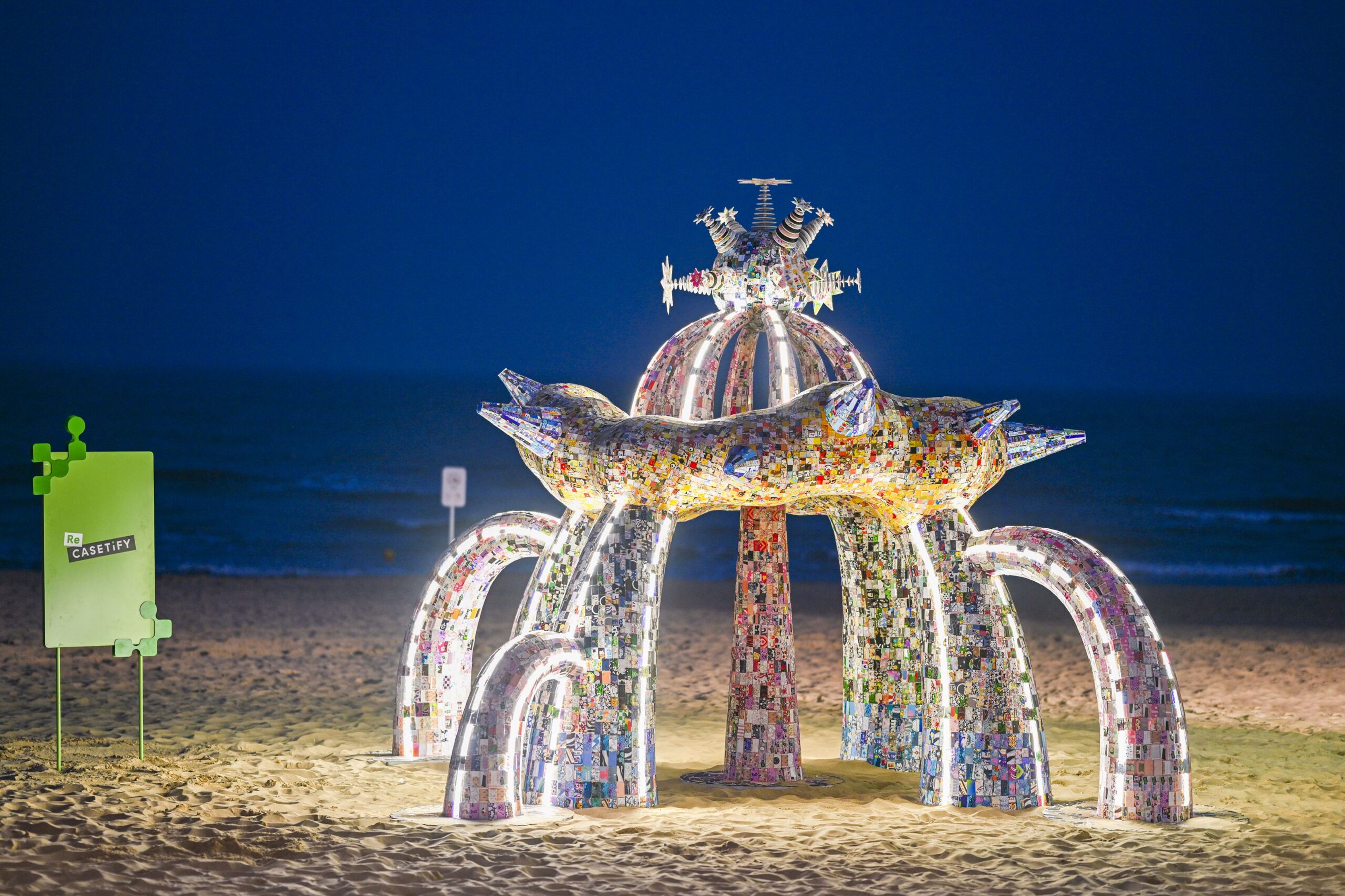 Illuminated sculpture made from recycled phone cases on the beach at dusk