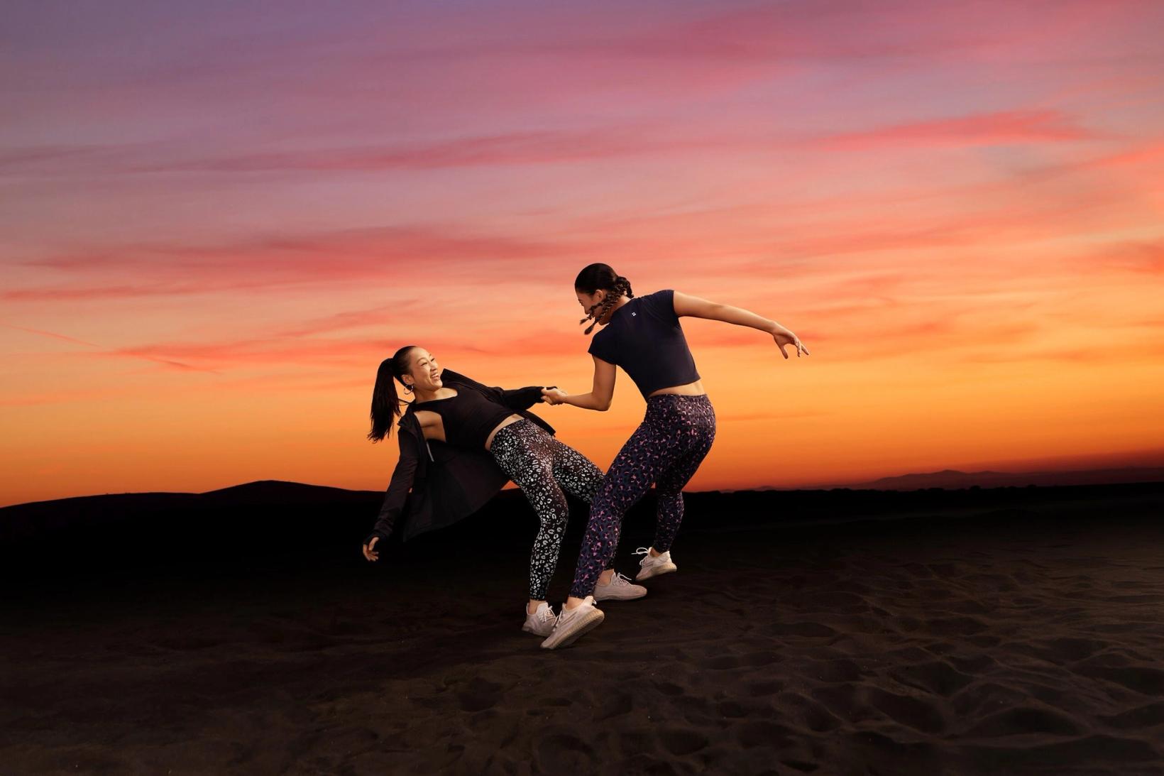 Two women training on dark sand under a sunset sky