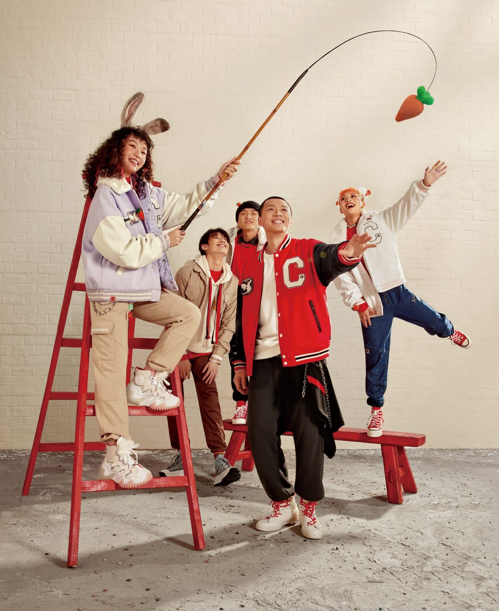 Four friends in Converse varsity jackets and bunny ears posing around a red ladder and bench