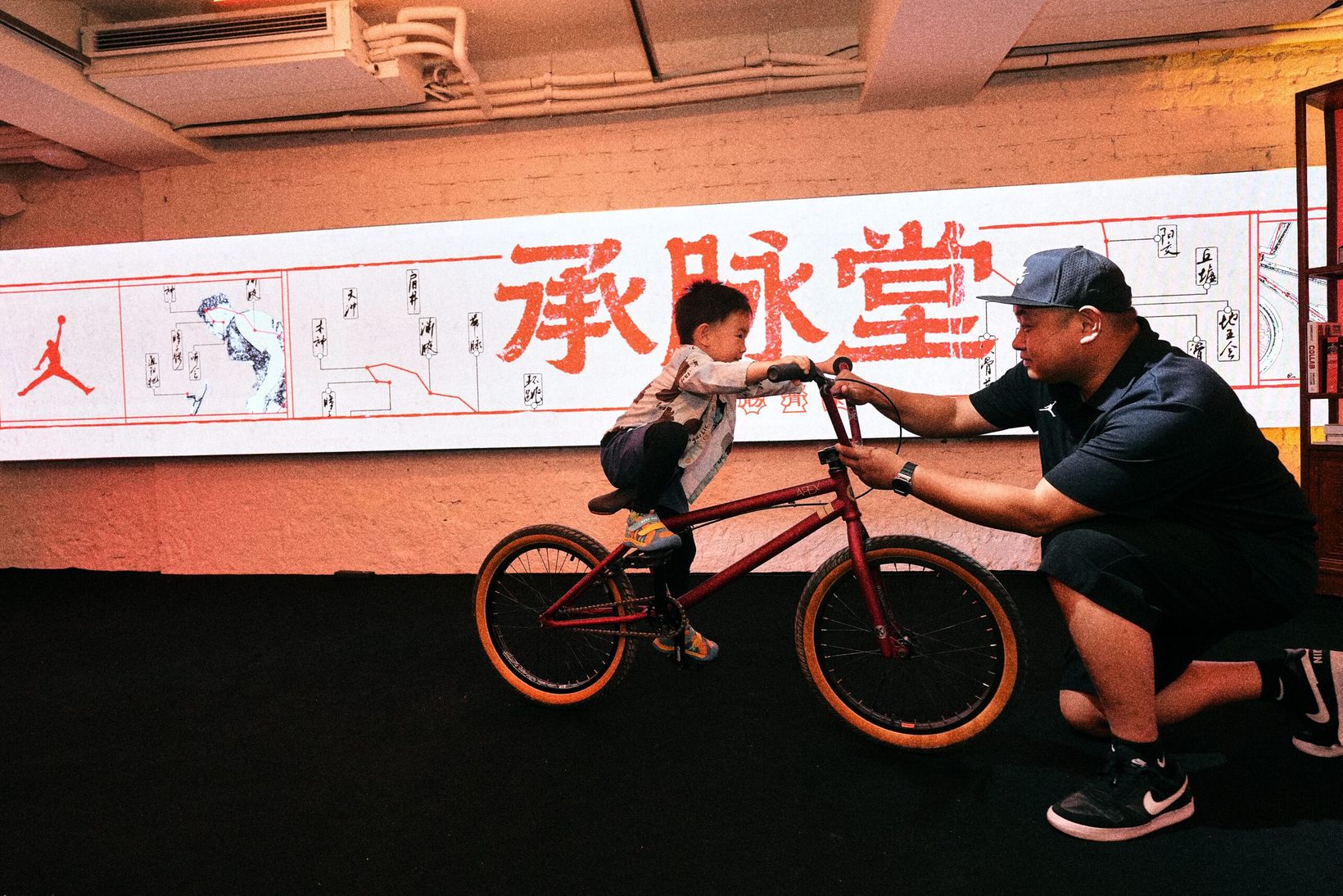 Mechanic adjusting a child's BMX bike in front of the Cheng Mai Tang mural