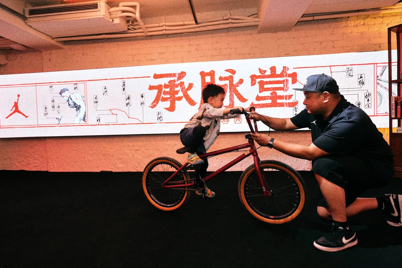 Mechanic adjusting a child's BMX bike in front of the Cheng Mai Tang mural