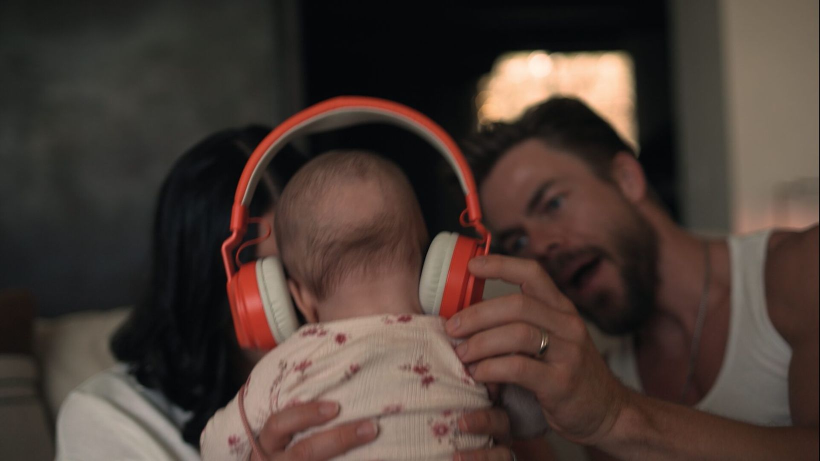 Derek Hough holding his baby wearing orange headphones
