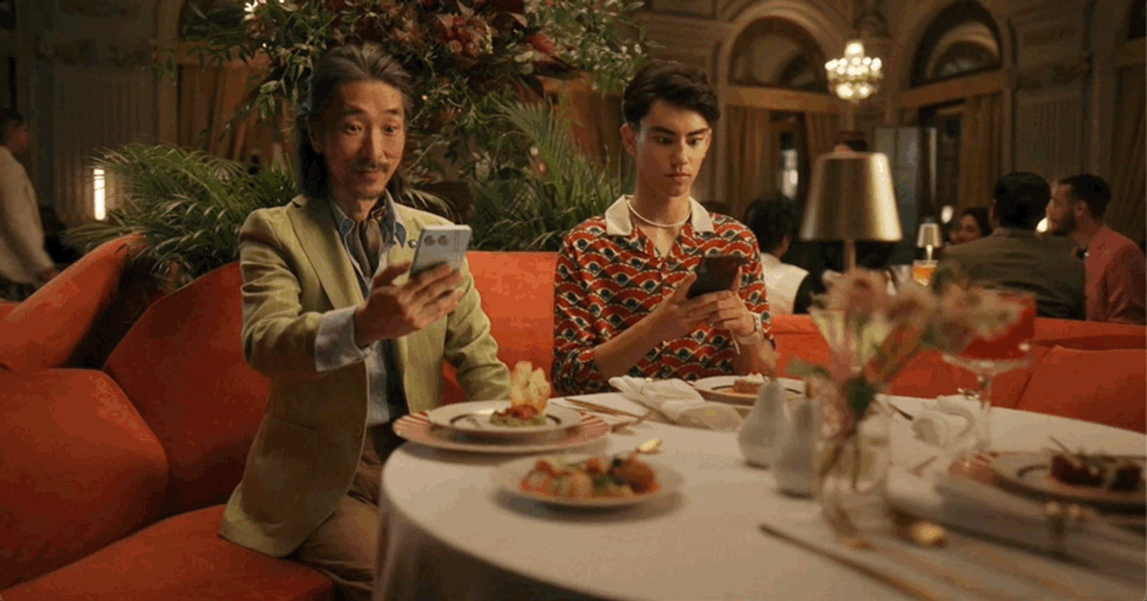 Diners on a red sofa looking at a phone at dinner