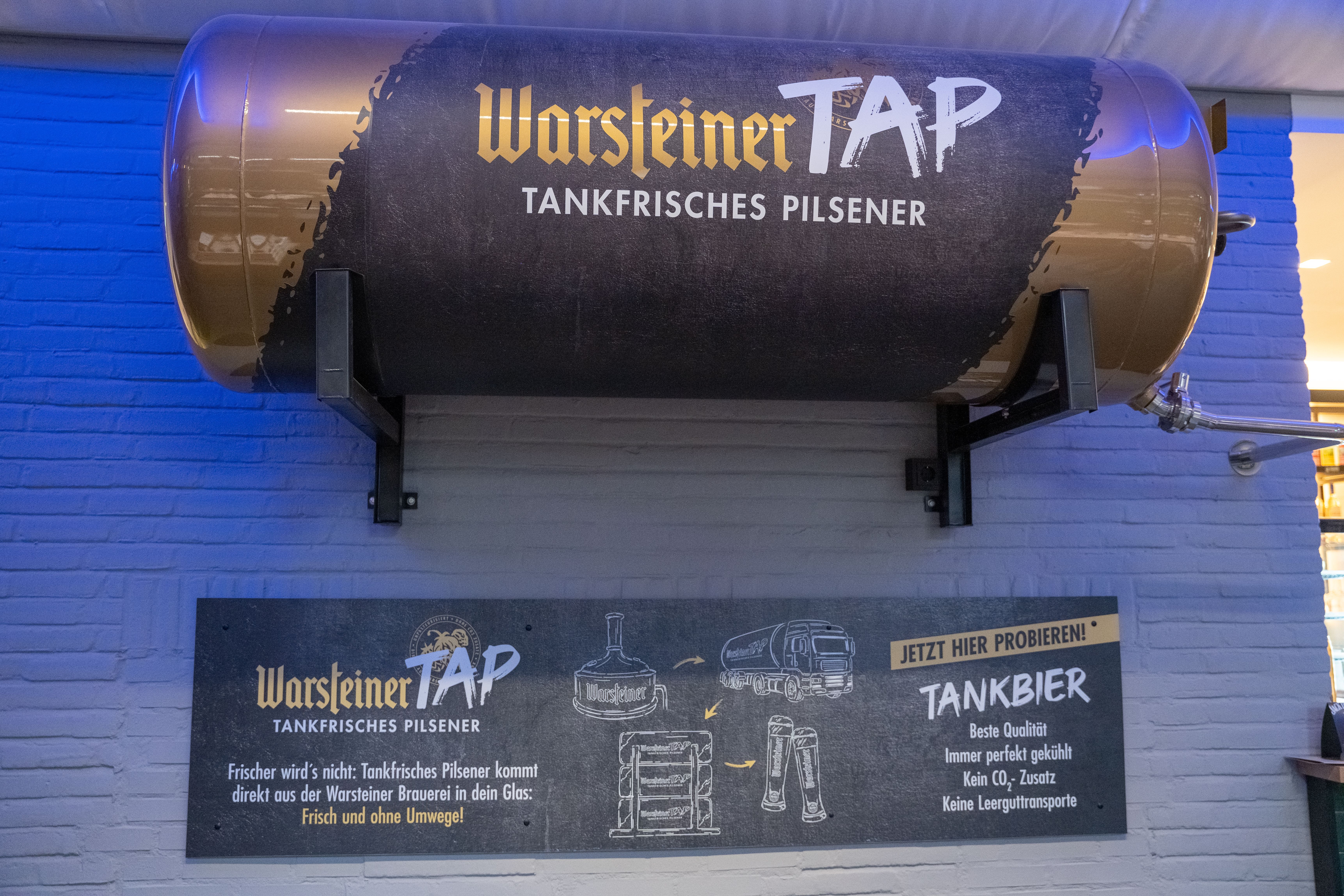 Warsteiner TAP Bierfass-Zapfanlage an der Wand der Wetthalle Neuss mit Infotafel zu tankfrischem Pilsener ohne CO₂-Zusatz