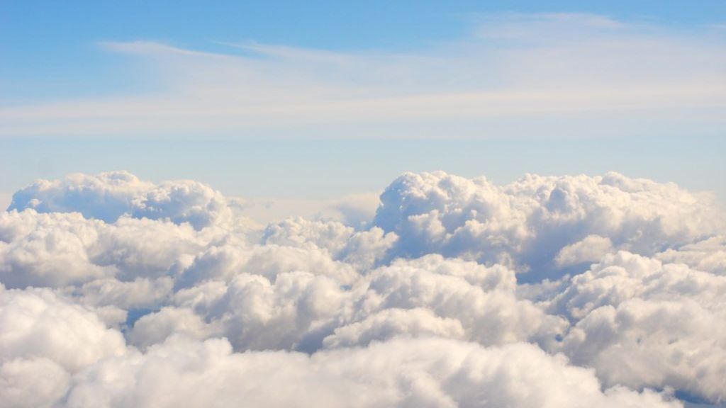 Een uitgestrekt wolkendek van bovenaf gezien, onder een open blauwe hemel.