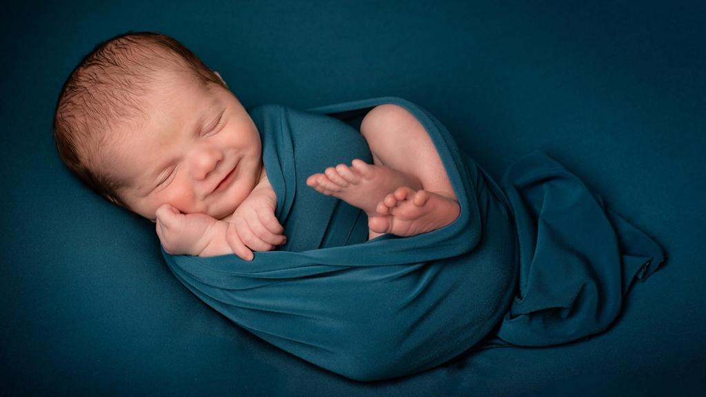 Een pasgeboren baby, slapend en ingebakerd in een diepblauwe doek.