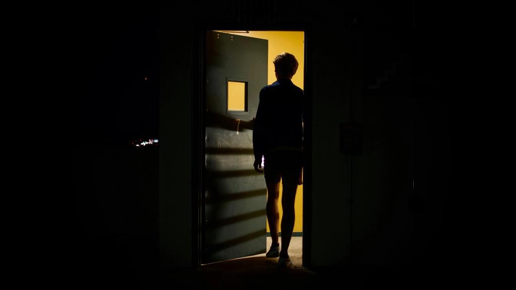 Een figuur in een donkere kamer die een deur opent naar warm, goudkleurig licht.