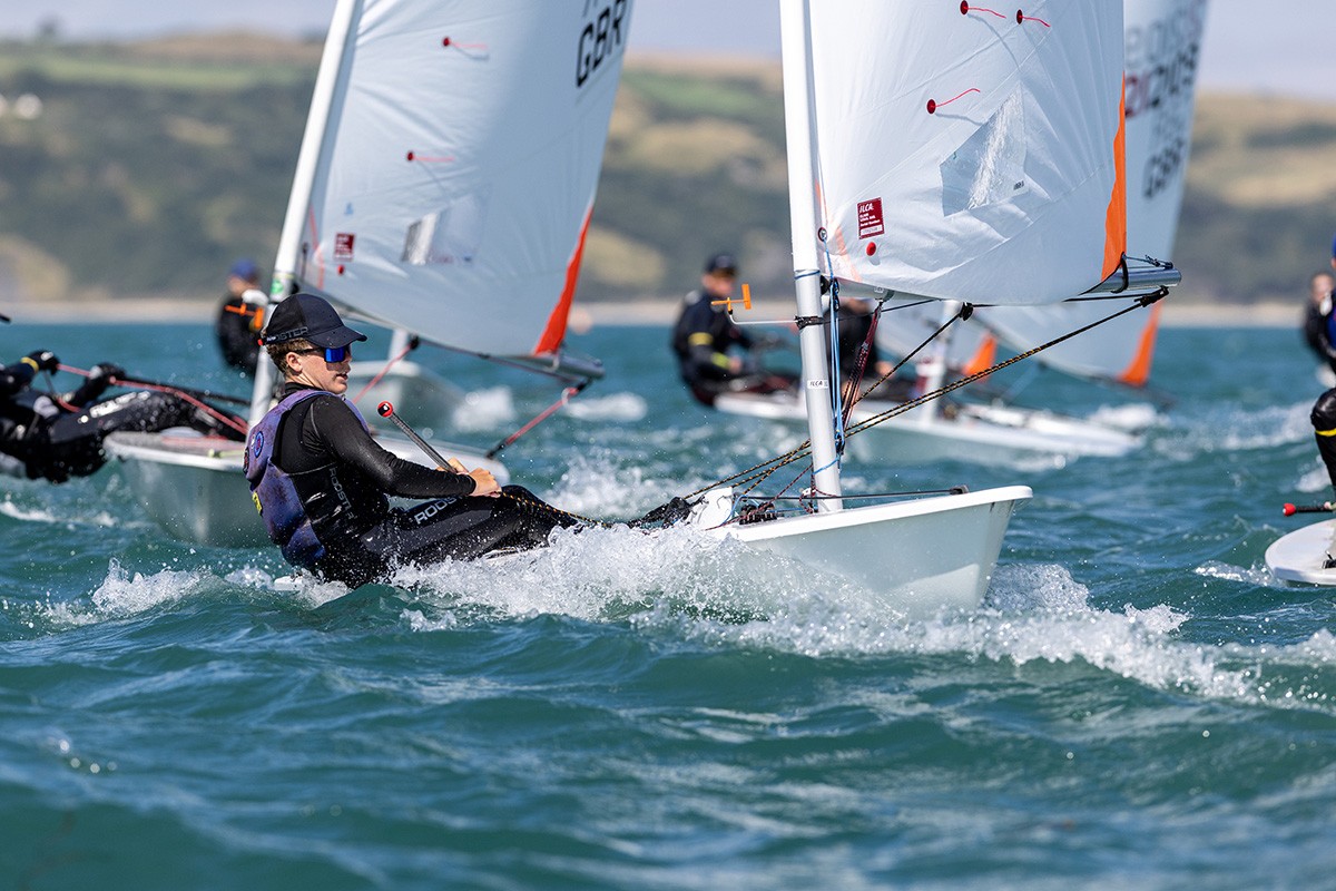 Multiple sailing competitors leaning back on their sailboats.
