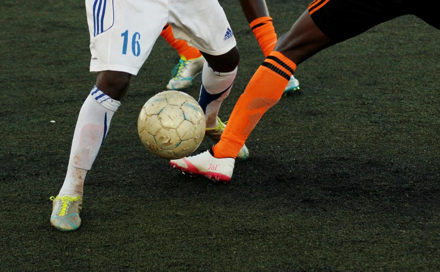 Two football players from opposing teams attempting to get the ball from one another on a football pitch. 