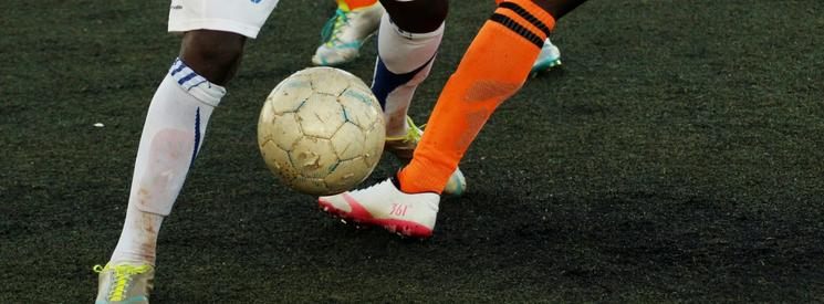 Two football players from opposing teams attempting to get the ball from one another on a football pitch. 