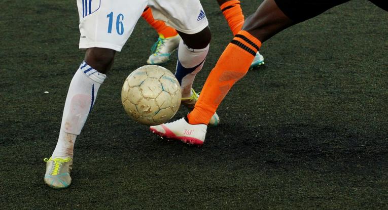 Two football players from opposing teams attempting to get the ball from one another on a football pitch. 