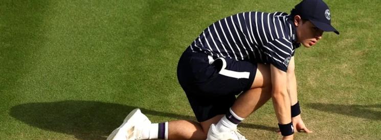 Tennis ball boy in a stripe T-Shirt, black shorts and white tennis shoes uniform crouched over on the sideline of a tennis match.