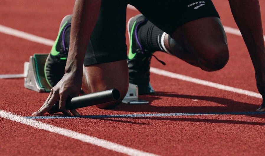 A close up shot of athlete preparing for a sprint track race by placing their feet on clocks and positioning their hands on the track line.