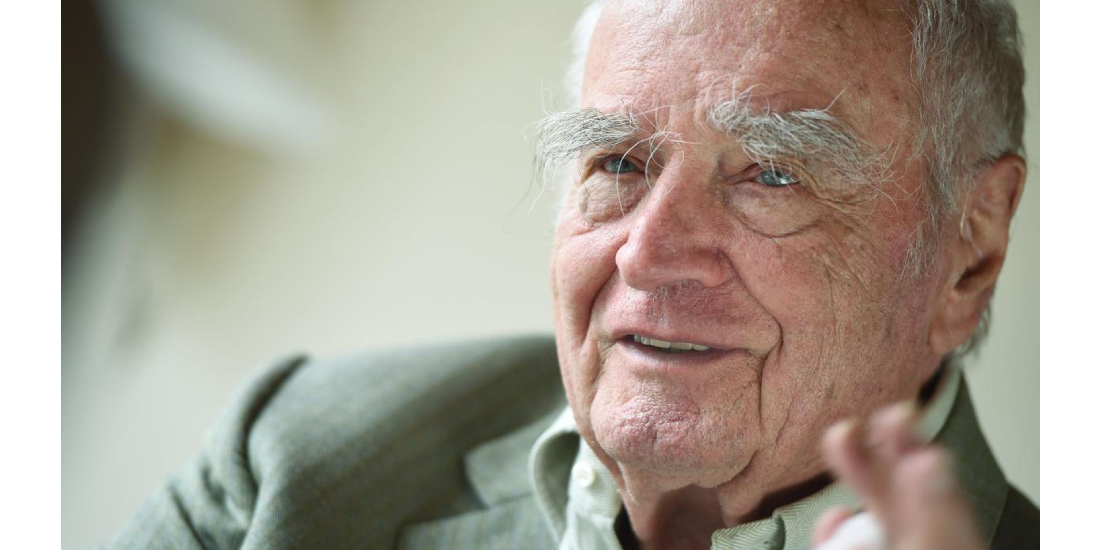 Elderly man with white hair and prominent eyebrows, smiling.