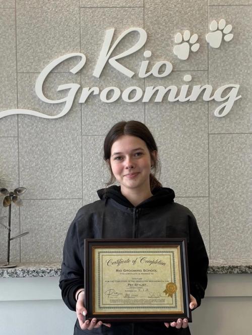 A Rio Grooming School graduate holding her Pet Stylist certificate