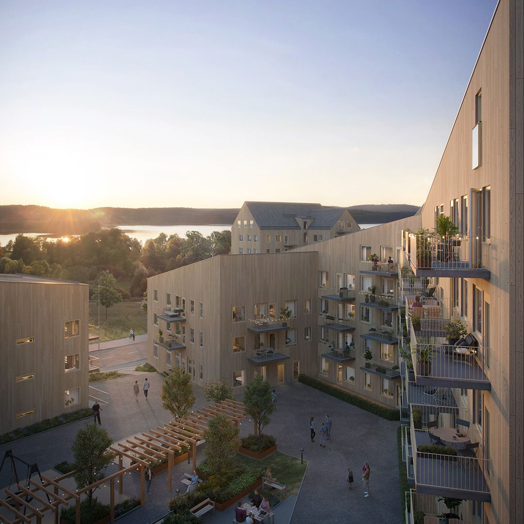 A tree apartment complex with balconys towards a courtyard with benches and green trees. A lake and sunrise in the foreground