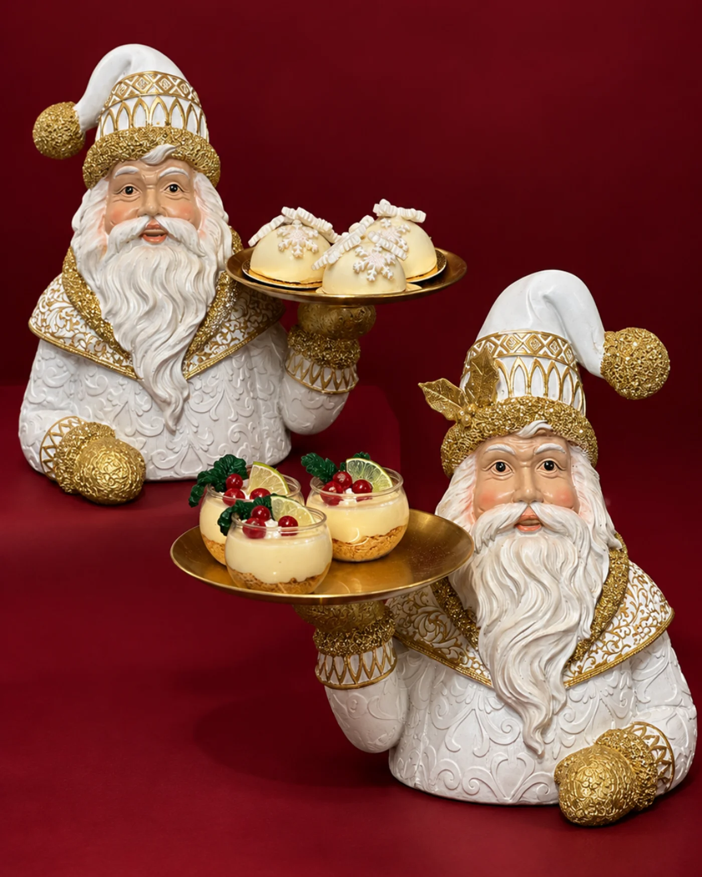 Dos figuras navideñas sostienen bandejas doradas con alimentos decorativos en una composición escalonada.