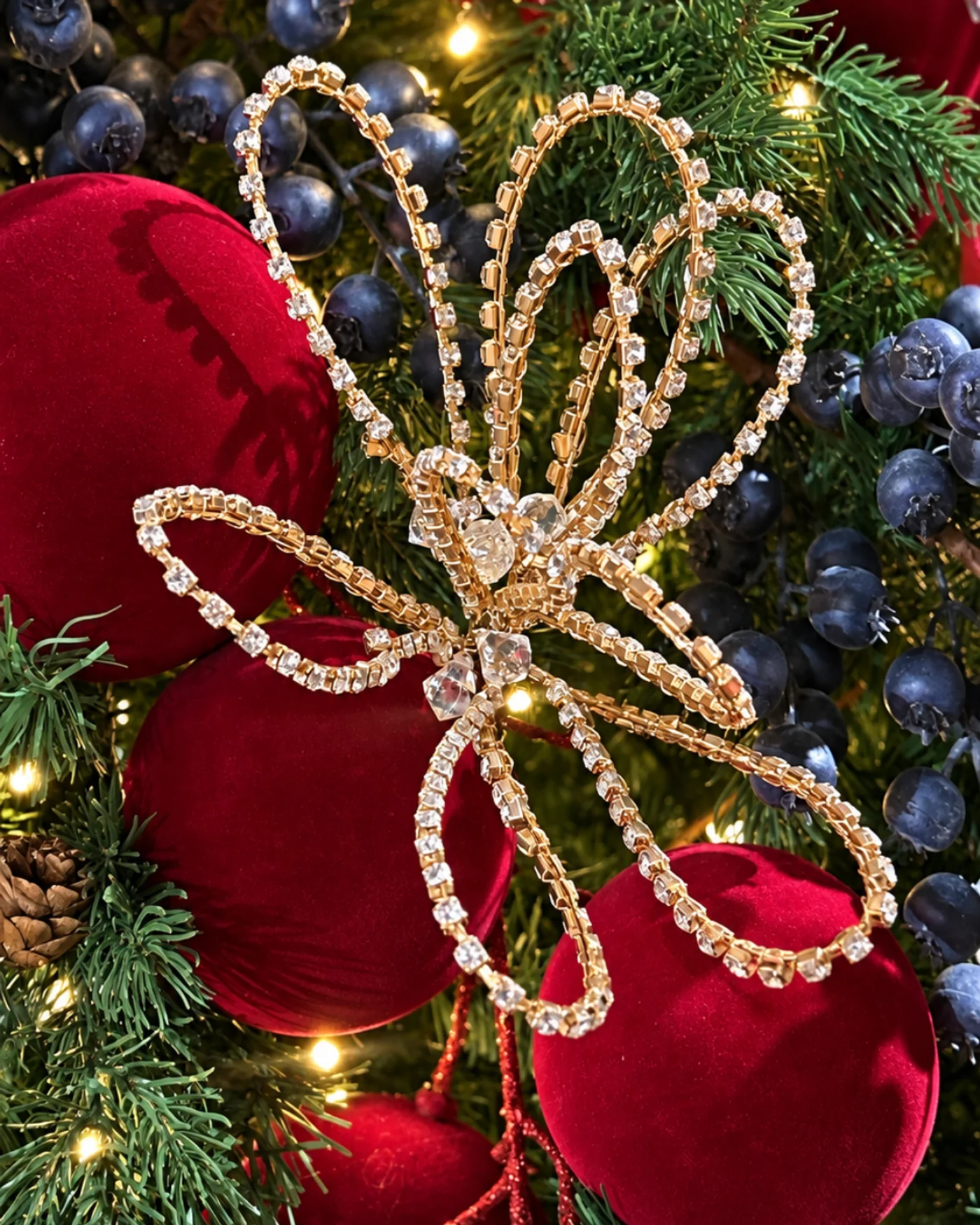 Detalle de árbol navideño con cinta roja y dorada, cuentas colgantes, flor roja y adornos.