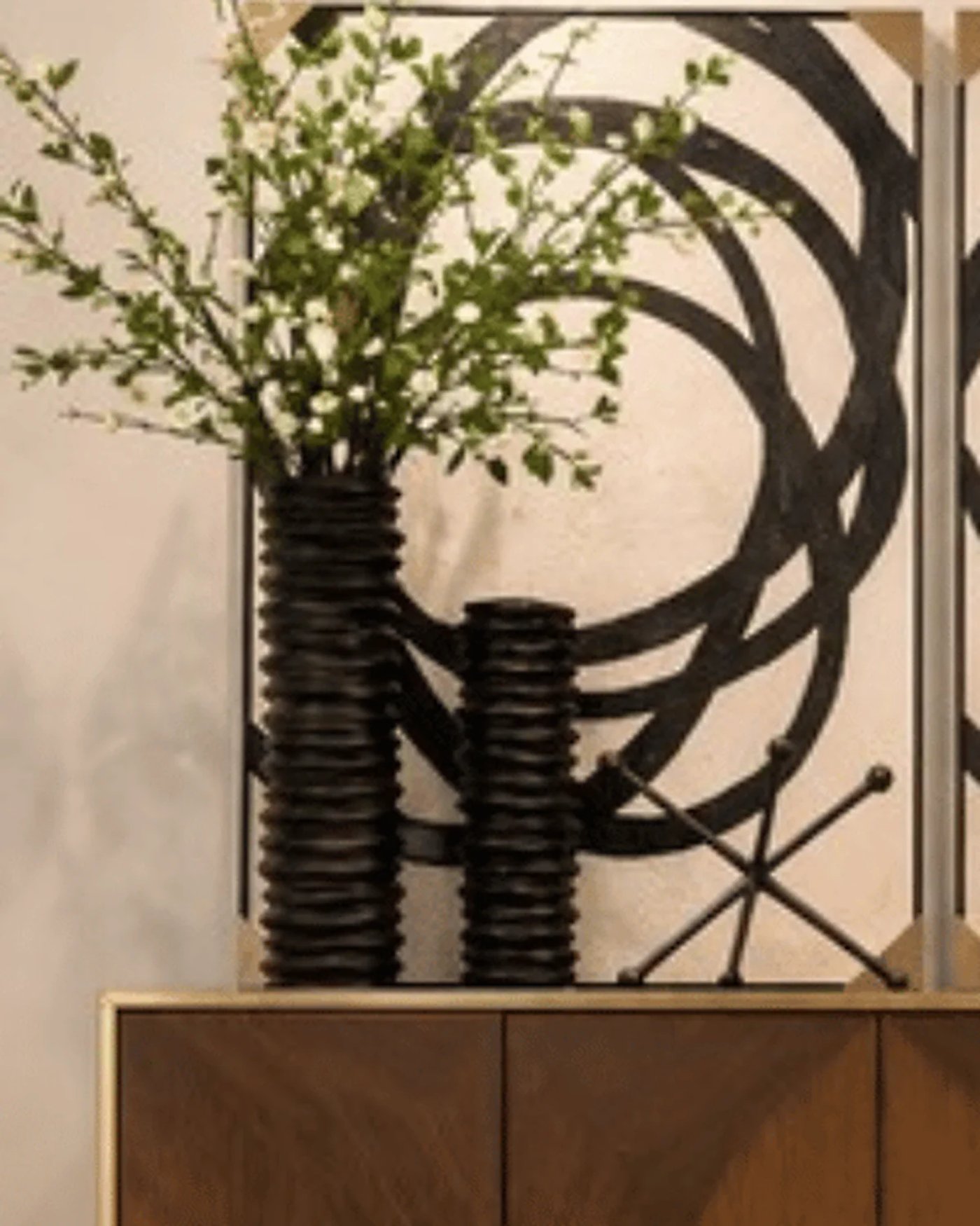 Dos jarrones negros de diferentes alturas con ramas, ubicados sobre un mueble.