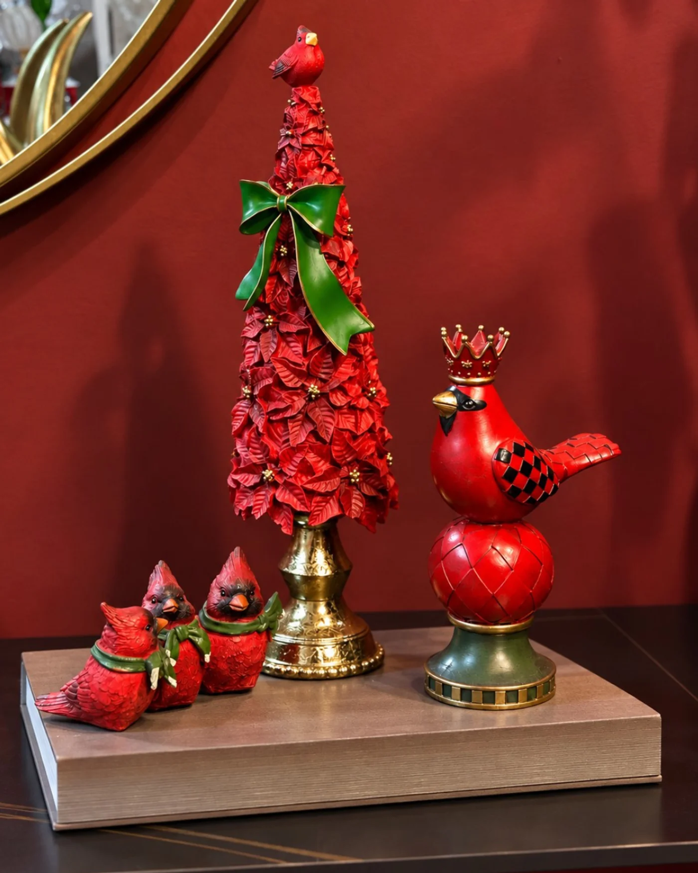 Árbol decorativo rojo pequeño con lazo verde sobre una consola junto a adornos rojos.