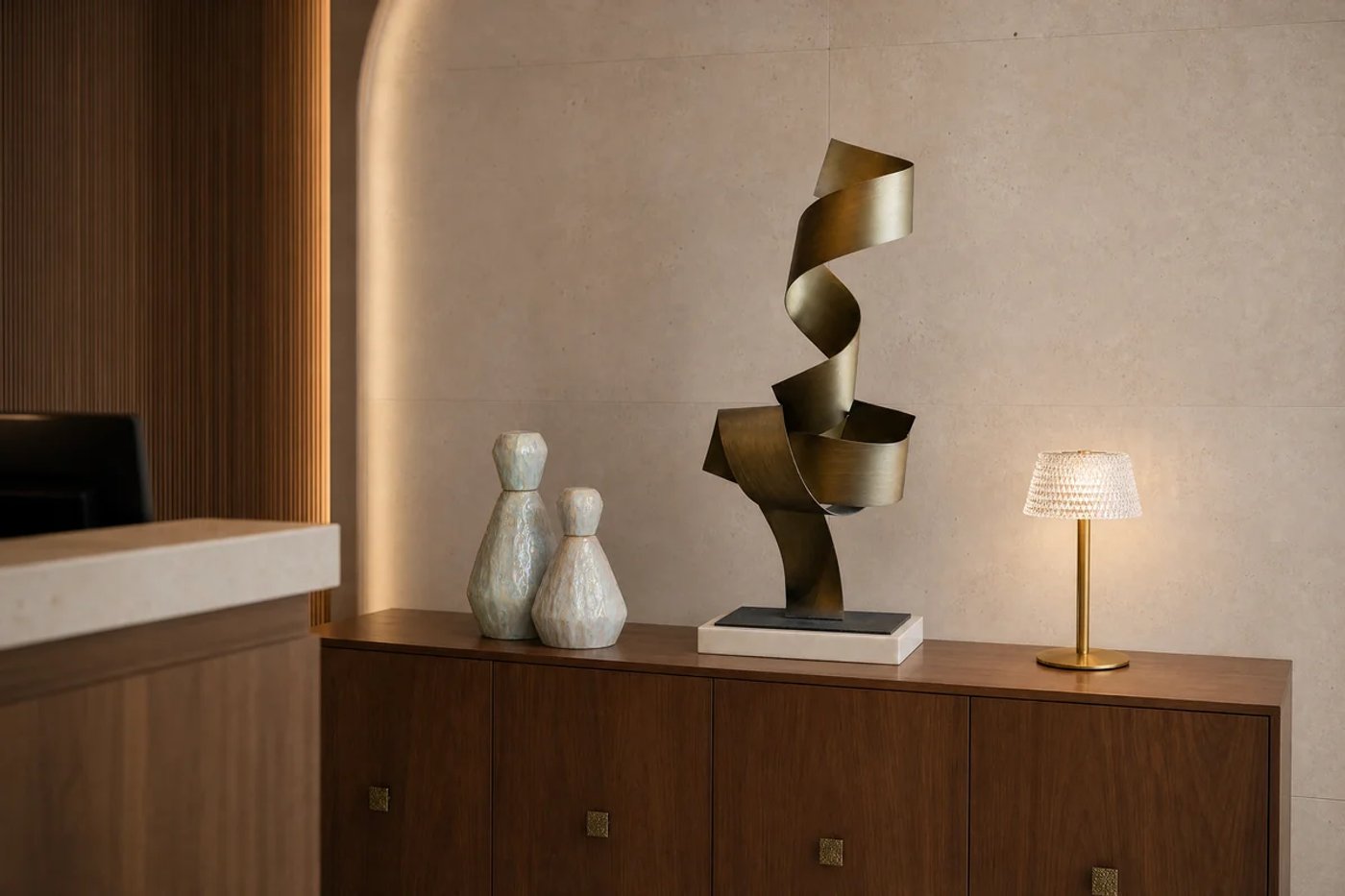 Recepción corporativa con escultura dorada, jarrones cerámicos, consola de madera y luz cálida.