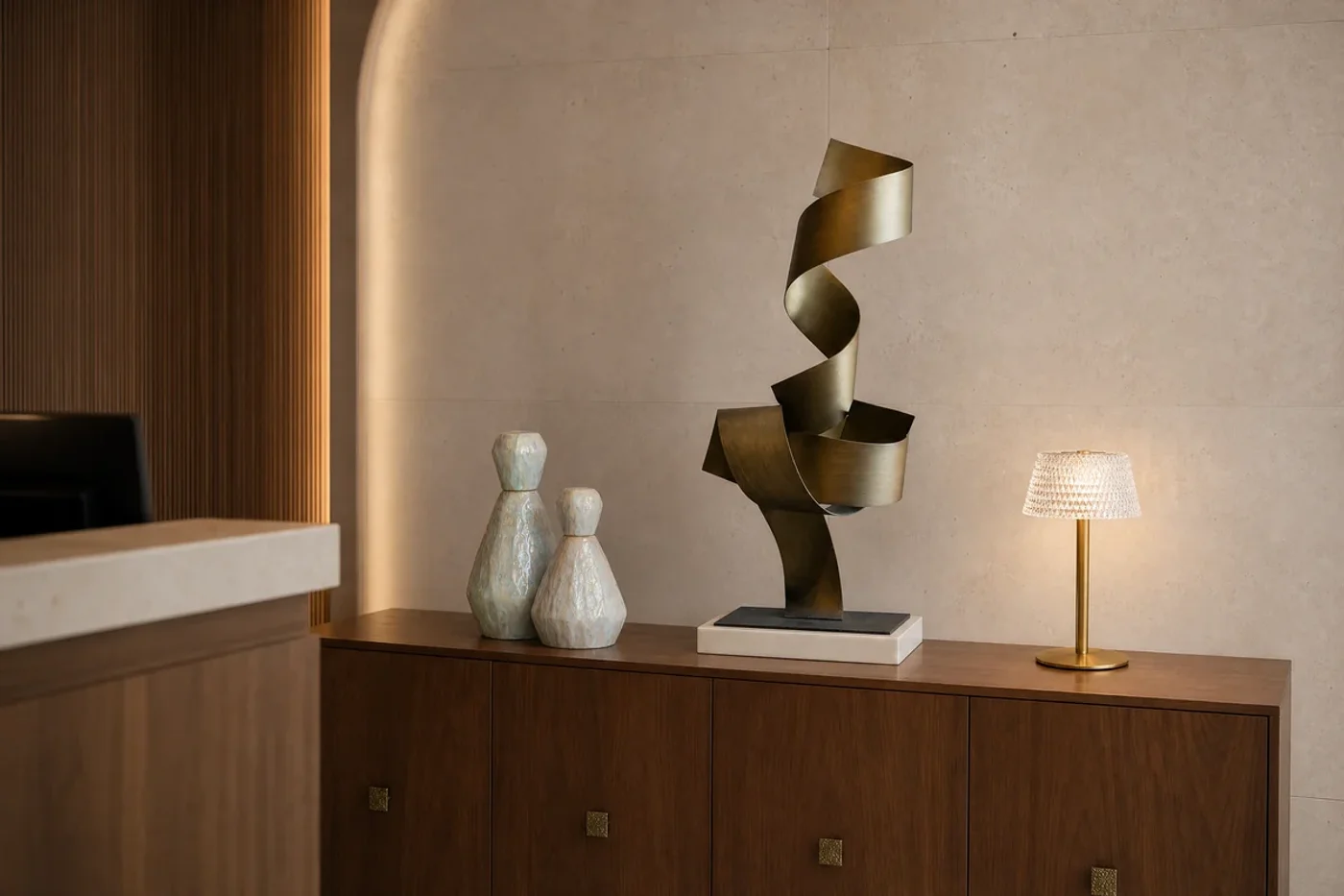 Recepción corporativa con escultura dorada, jarrones cerámicos, consola de madera y luz cálida.