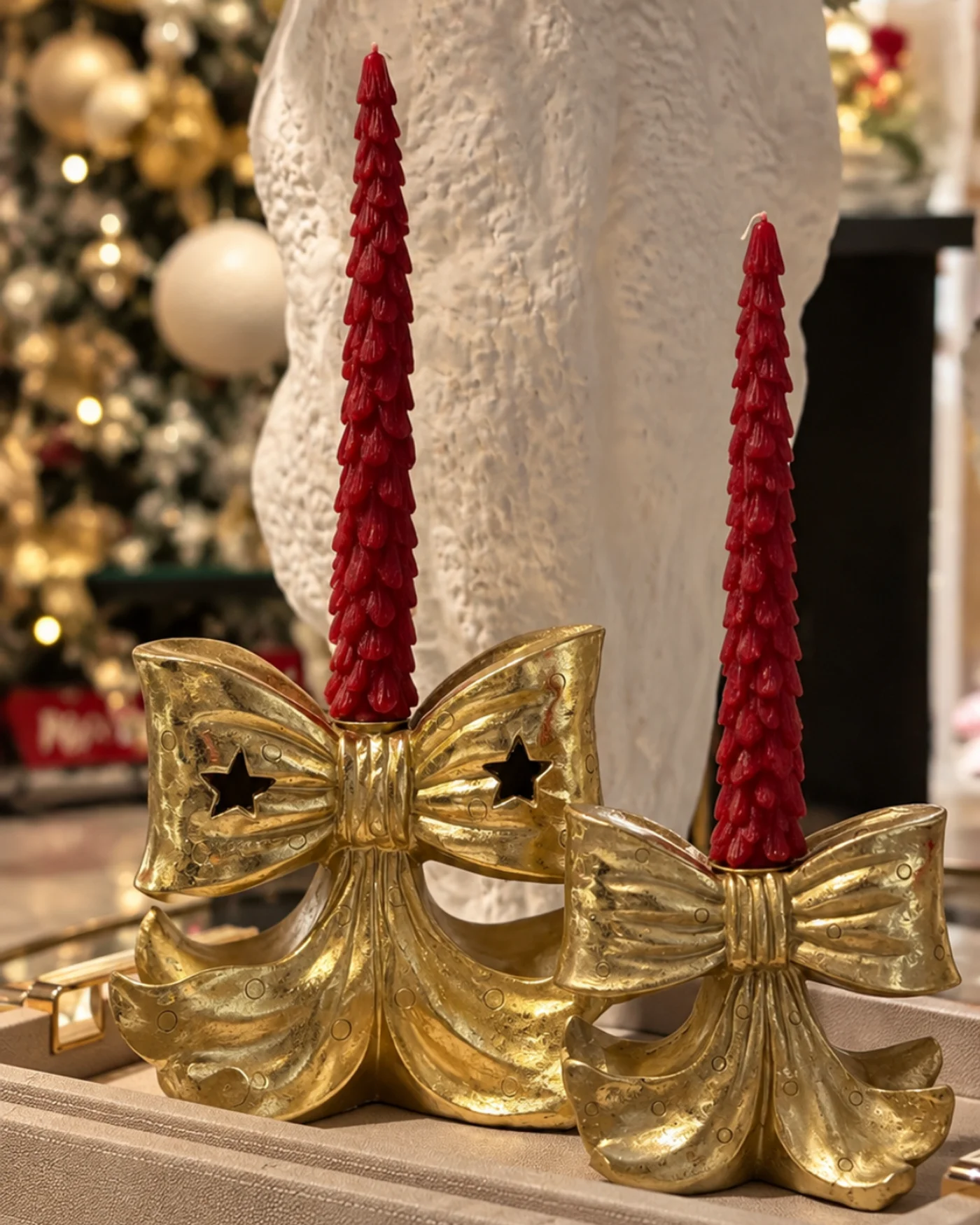 Dos portavelas dorados con velas rojas sobre una bandeja en una composición navideña compacta.