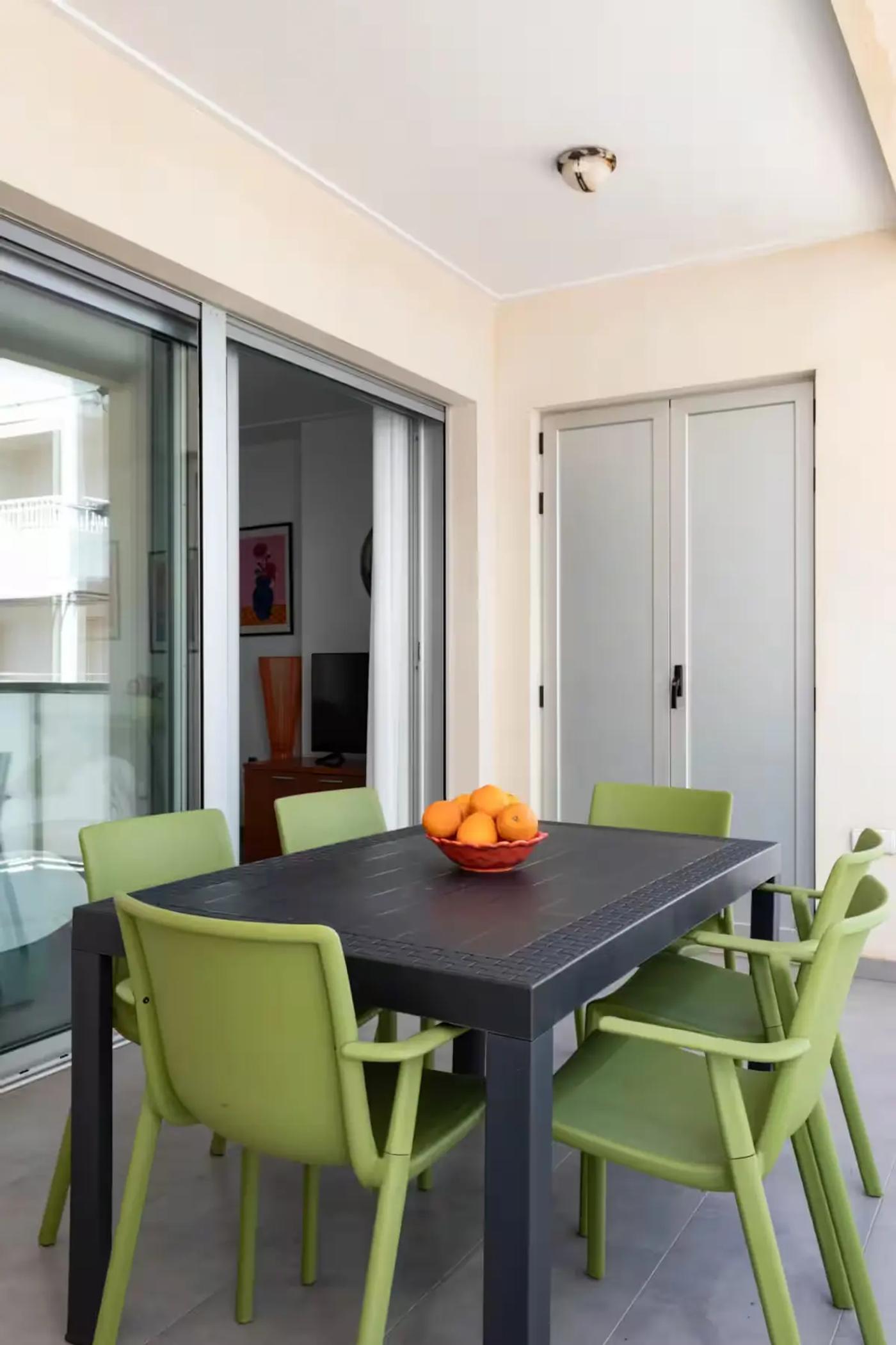 Mesa negra con seis sillas verdes y centro de mesa decorativo con naranjas en el balcón de la casa de la Playa de Miramar
