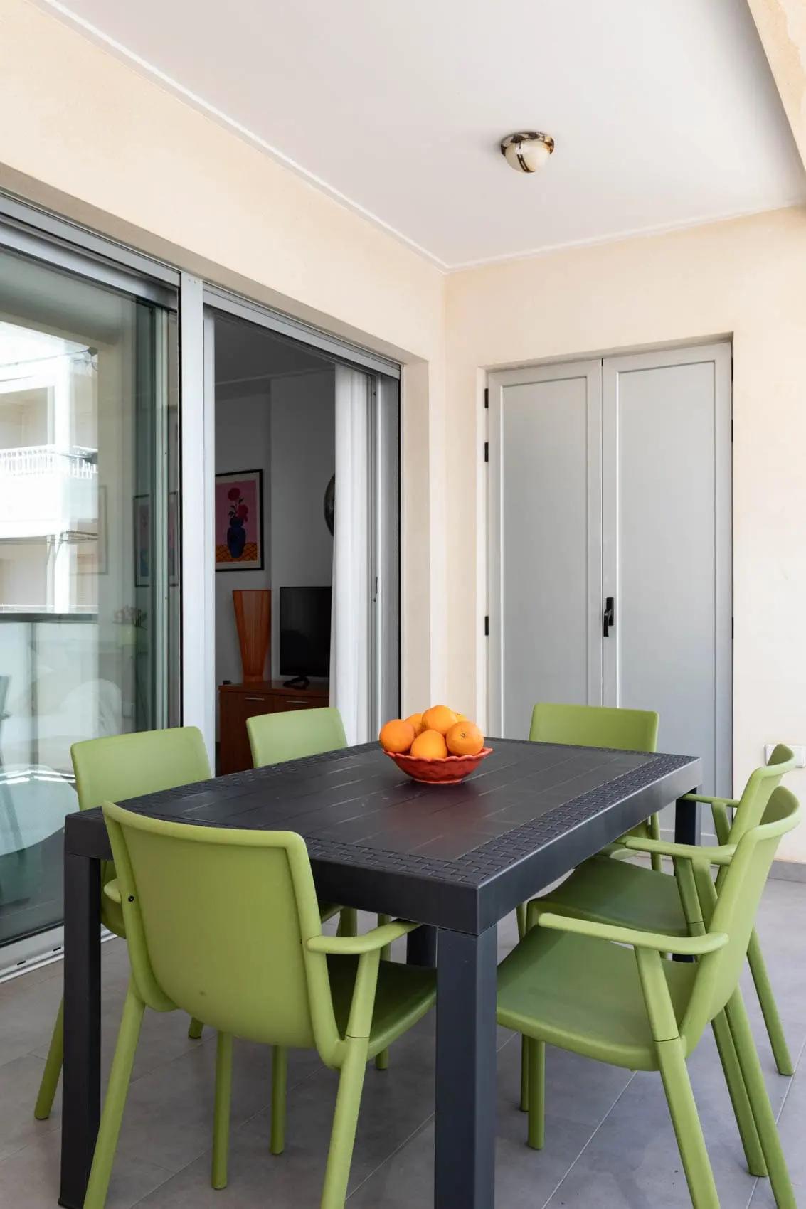 Mesa negra con seis sillas verdes y centro de mesa decorativo con naranjas en el balcón de la casa de la Playa de Miramar