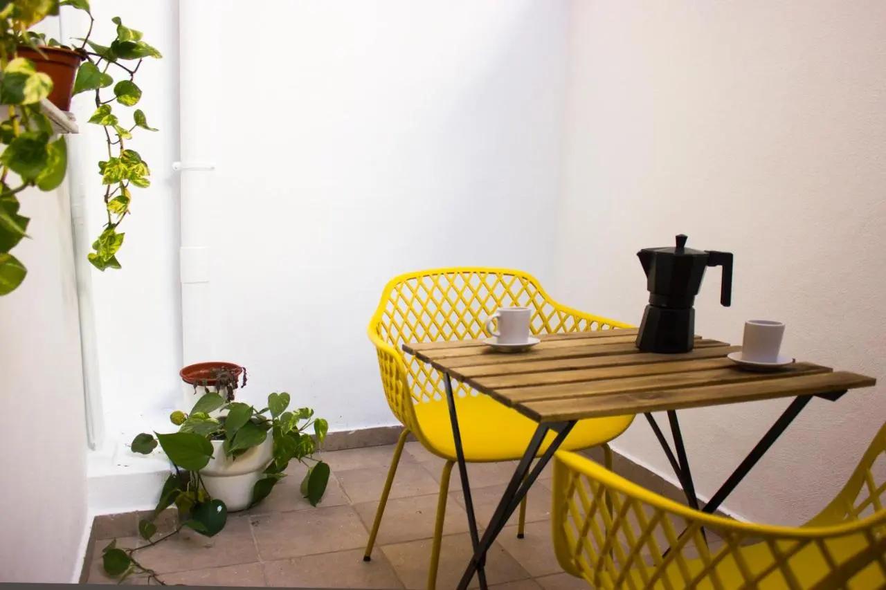 Mesa de madera con cafetera italiana y dos tazas de café, con dos sillas amarillas, en el patio interno del apartamento del centro de Gandía