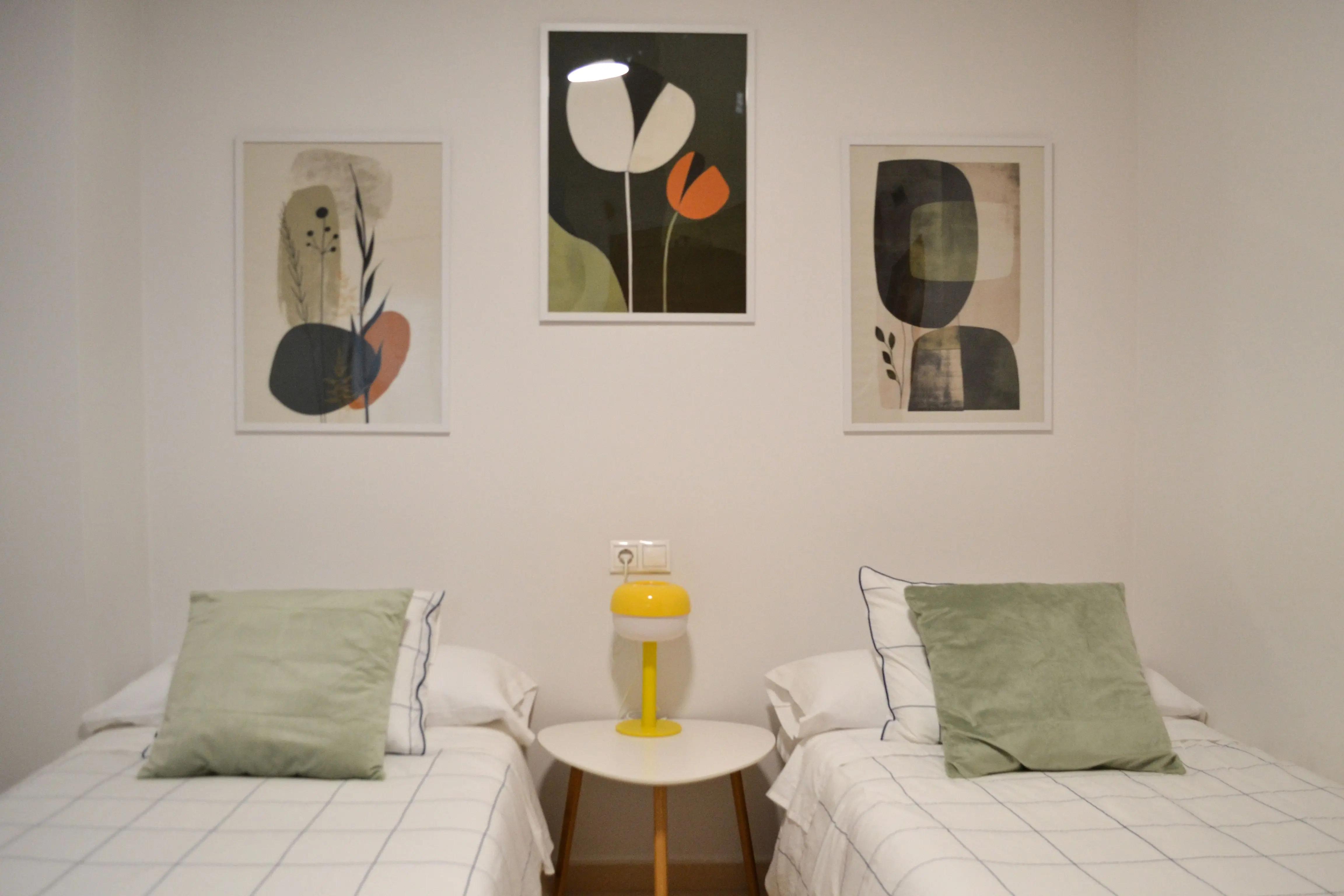 Vista frontal de dos camas individuales con almohadones decorativos y mesa de luz en medio