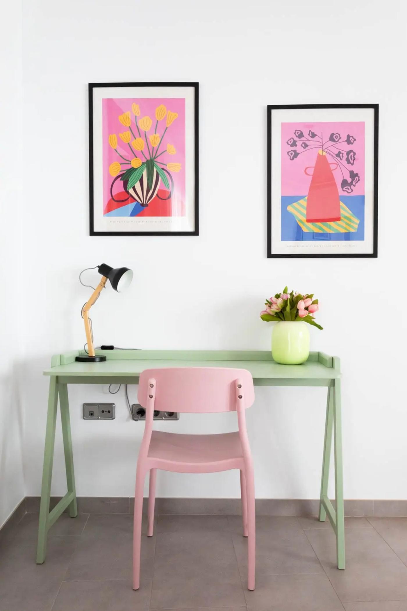 Escritorio verde con silla rosa, con lampara y florero sobre el escritorio