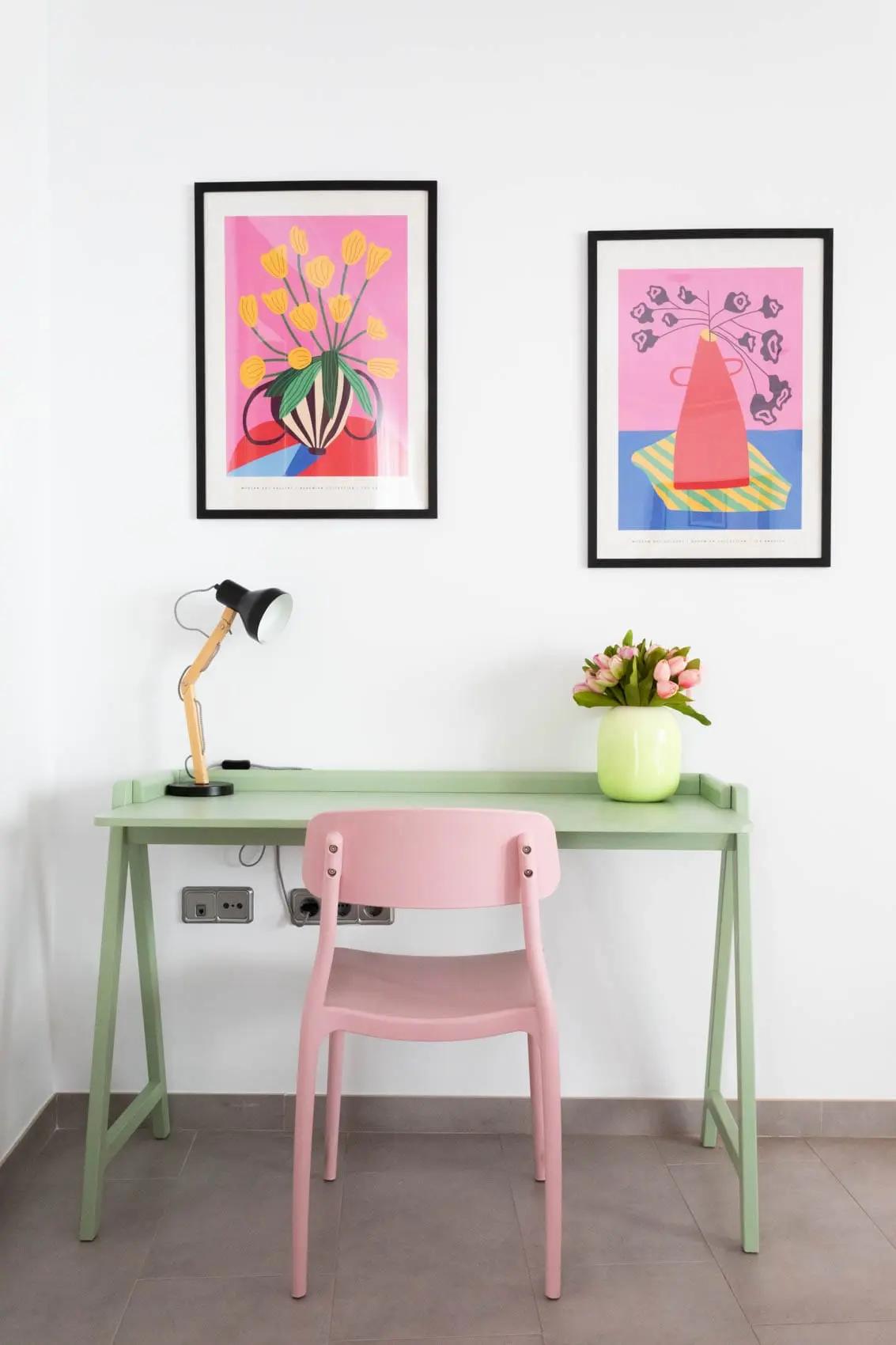 Escritorio verde con silla rosa, con lampara y florero sobre el escritorio