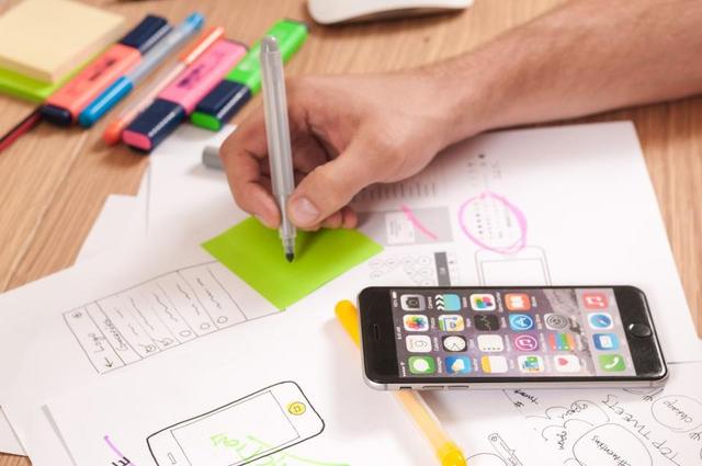 Bocetos de diseño web en papel junto a un celular, para comparar Elementor y Gutenberg