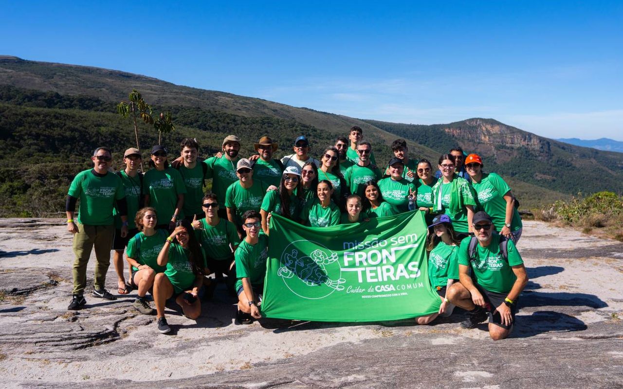 Participantes da Missão Sem Fronteiras 2025 posam com a bandeira do projeto em uma área montanhosa
