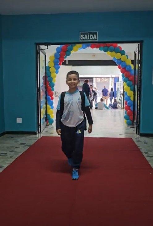 Estudante caminha por um tapete vermelho diante de um arco de balões na volta às aulas
