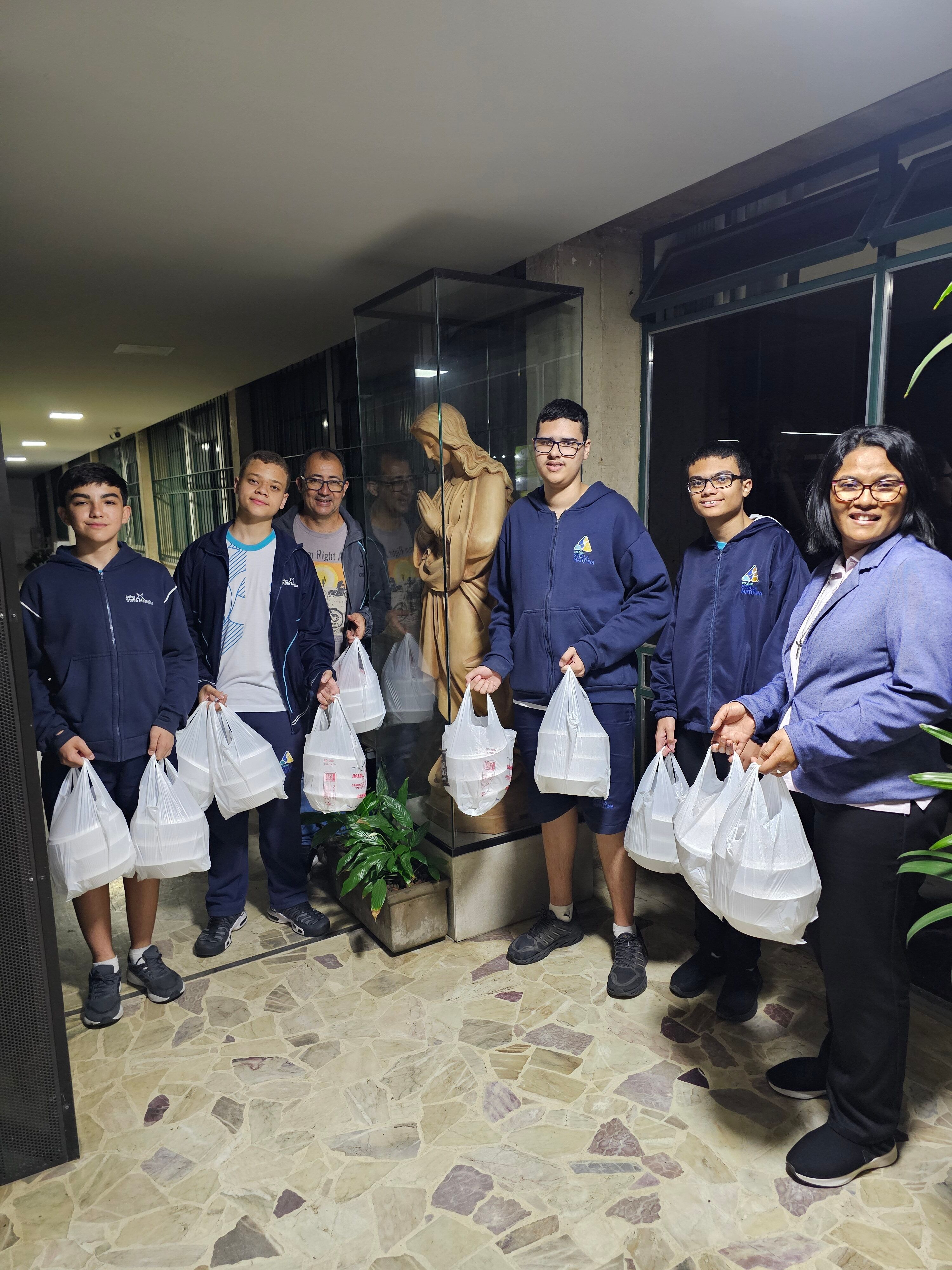 Estudantes da Juventude Missionária e educadores seguram sacolas com marmitas para a Ronda Noturna