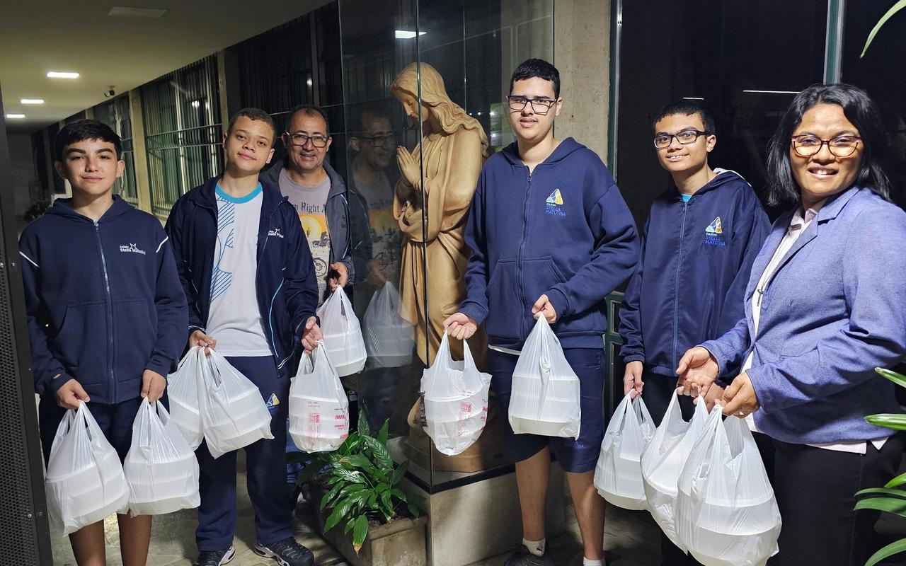 Estudantes da Juventude Missionária e educadores seguram sacolas com marmitas para a Ronda Noturna