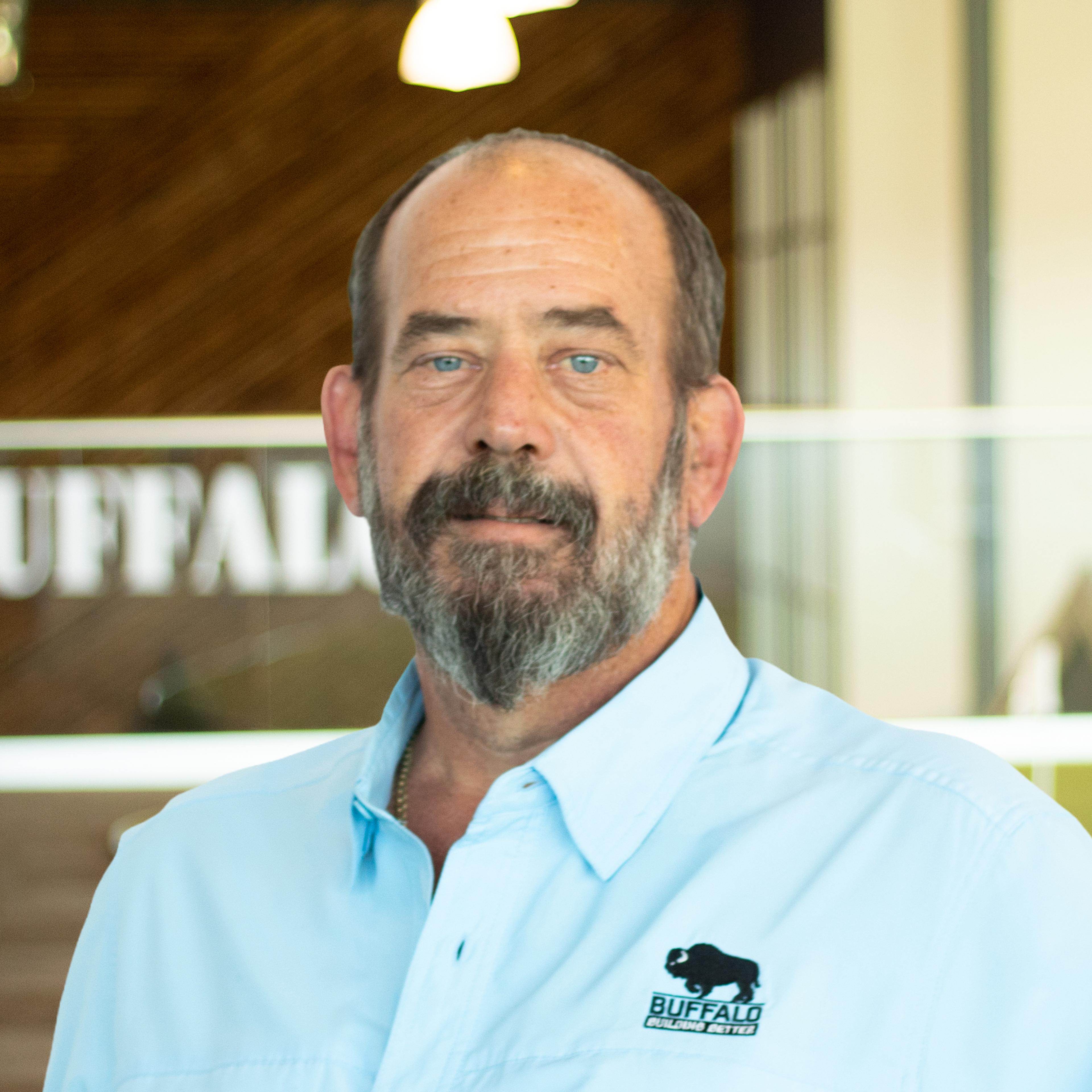 Mike Sparks smiling, wearing a light blue Buffalo Construction button-down shirt, standing in Buffalo Construction's office space.