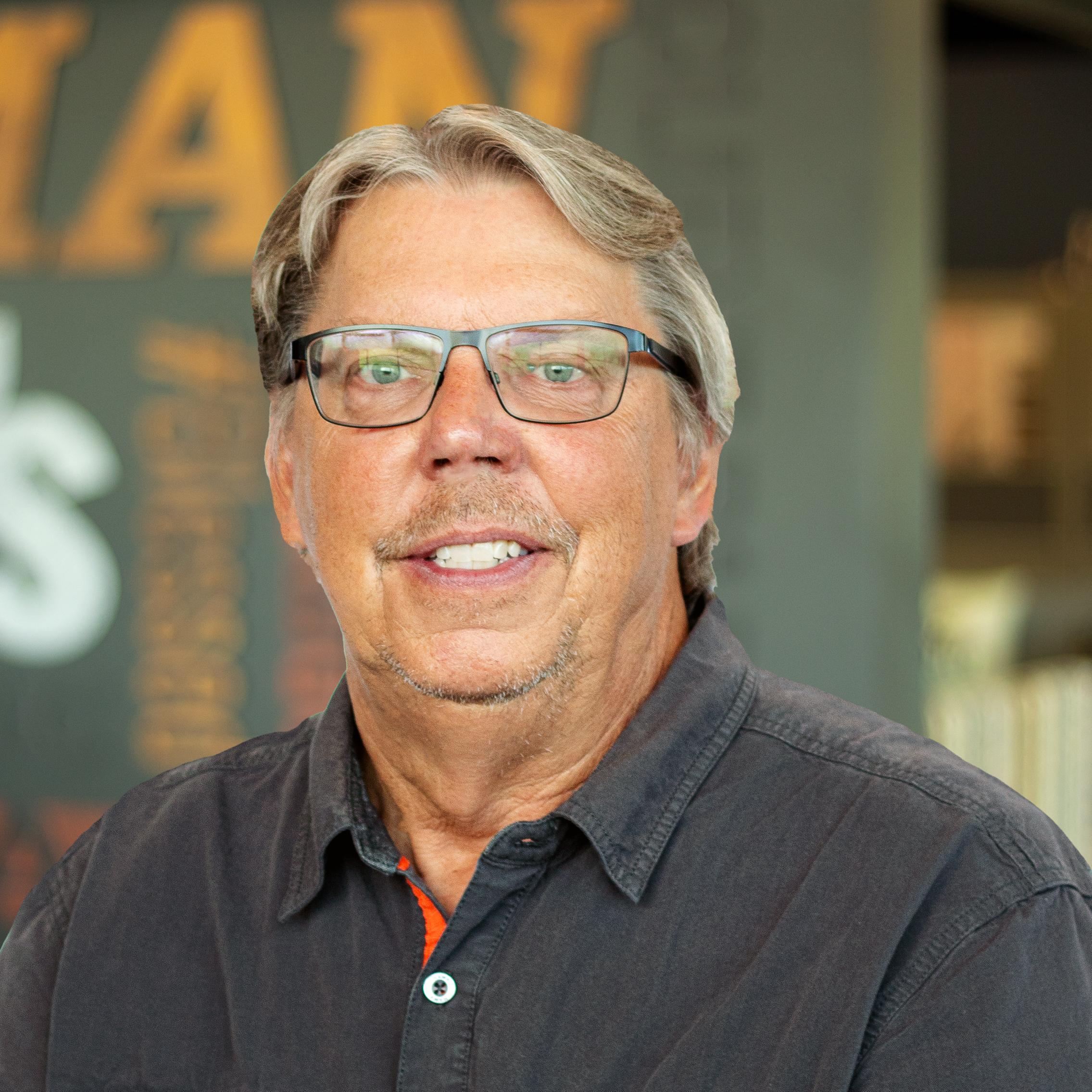 Kenny Walsh smiling and standing in front of a company-branded wall.