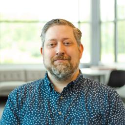 Joseph Hensel wearing a button down shirt and standing in a bright, modern office.