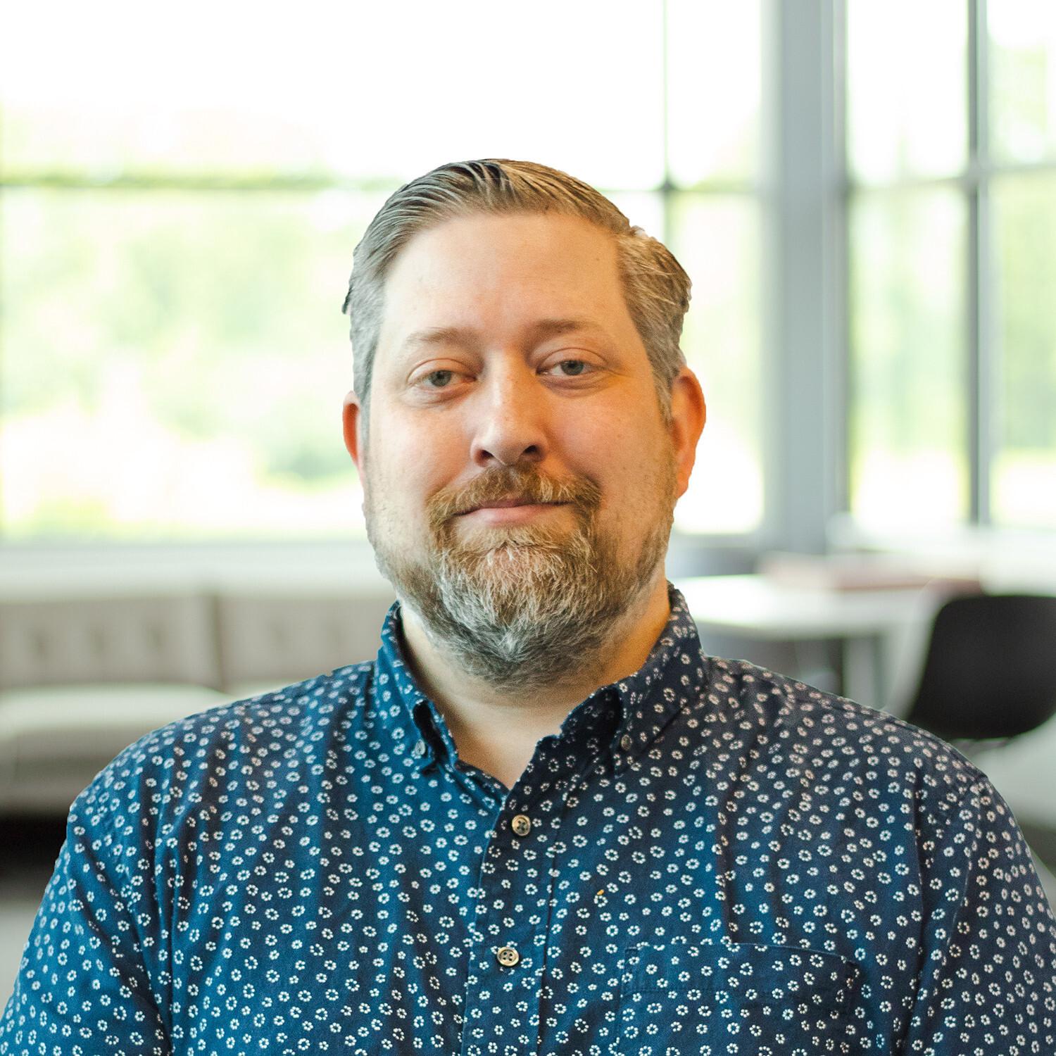 Joseph Hensel wearing a button down shirt and standing in a bright, modern office.