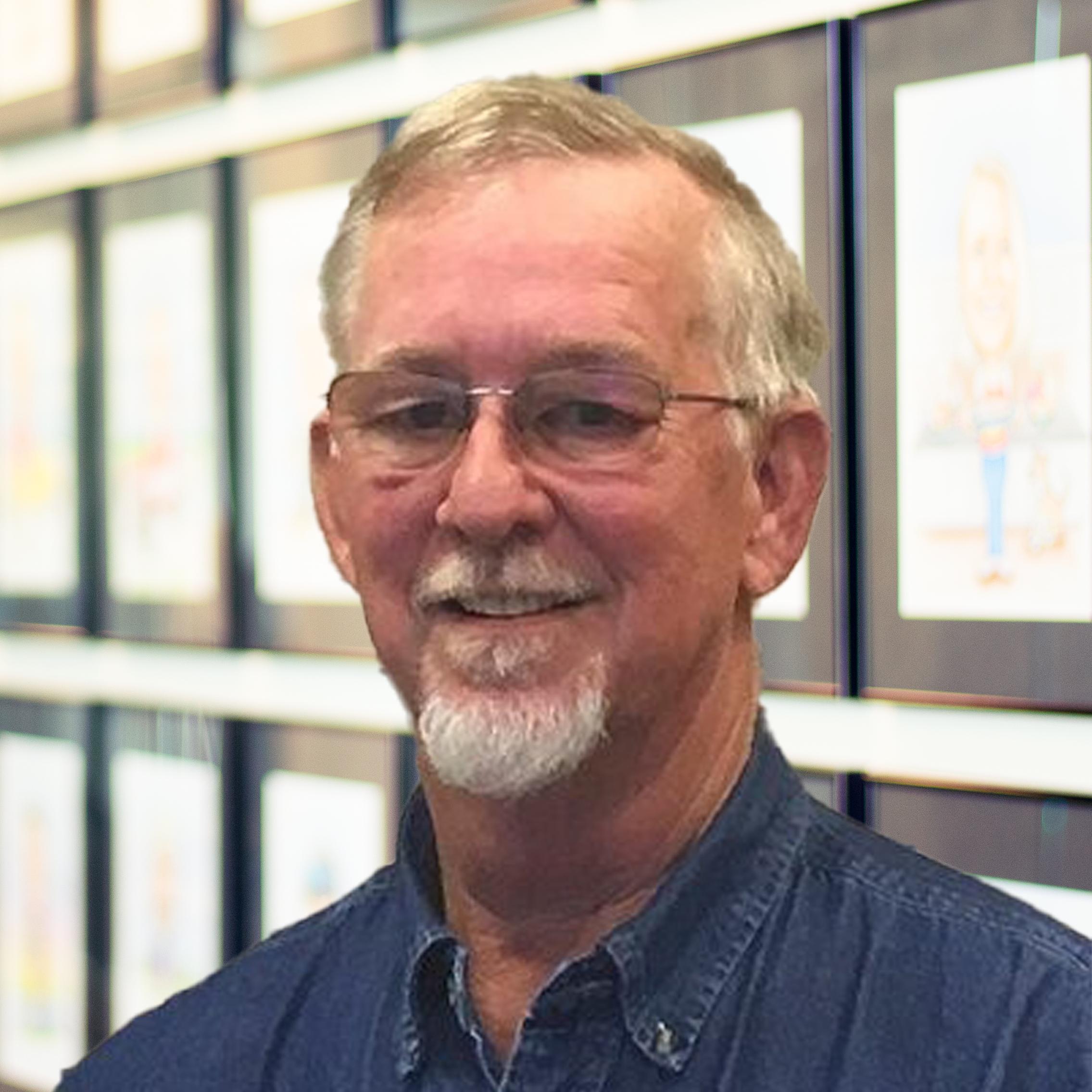 Rick Black wearing a smile, standing in front of a wall displaying framed caricatures.