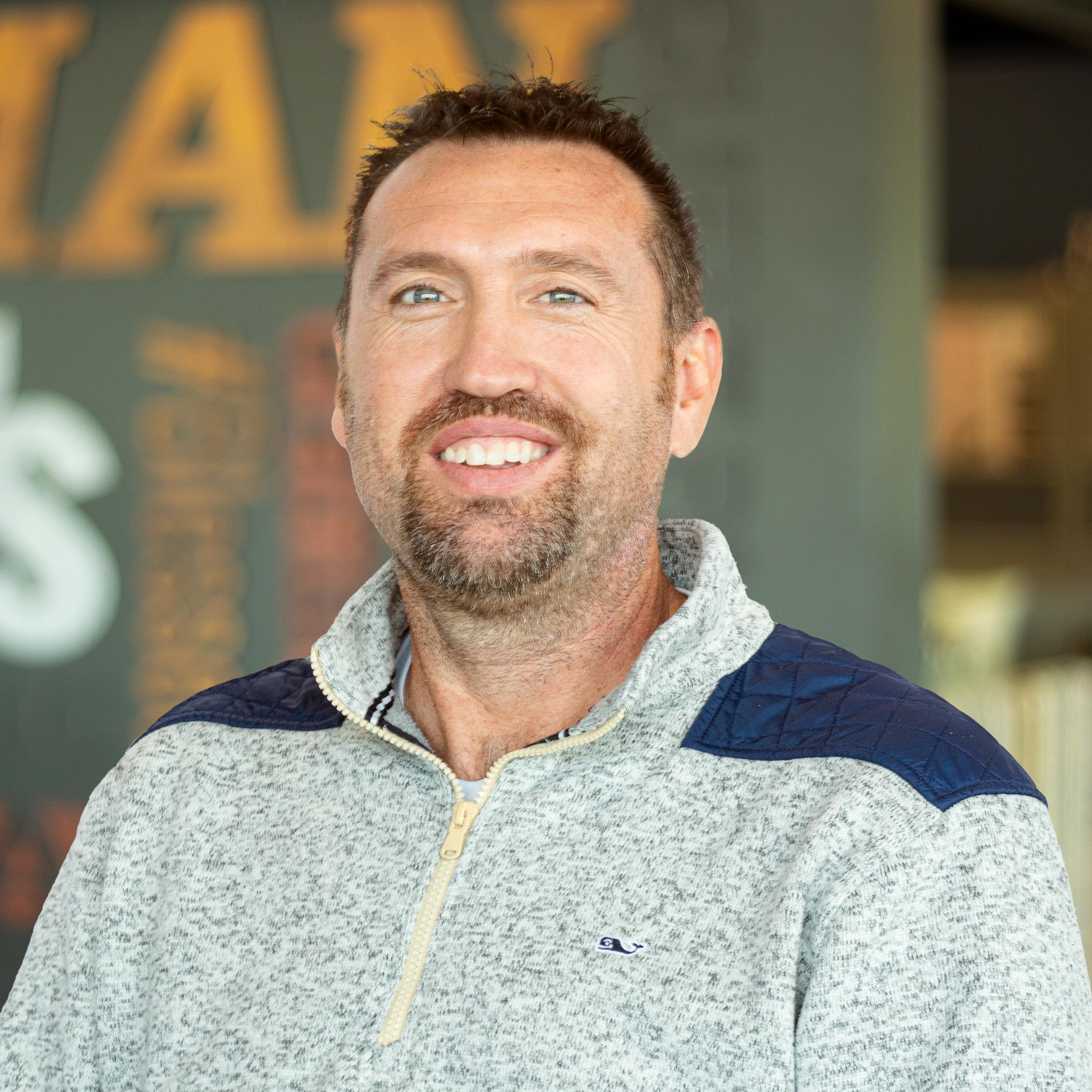 Nathan Rariden bright-eyed and smiling, standing in front of a company-branded wall.