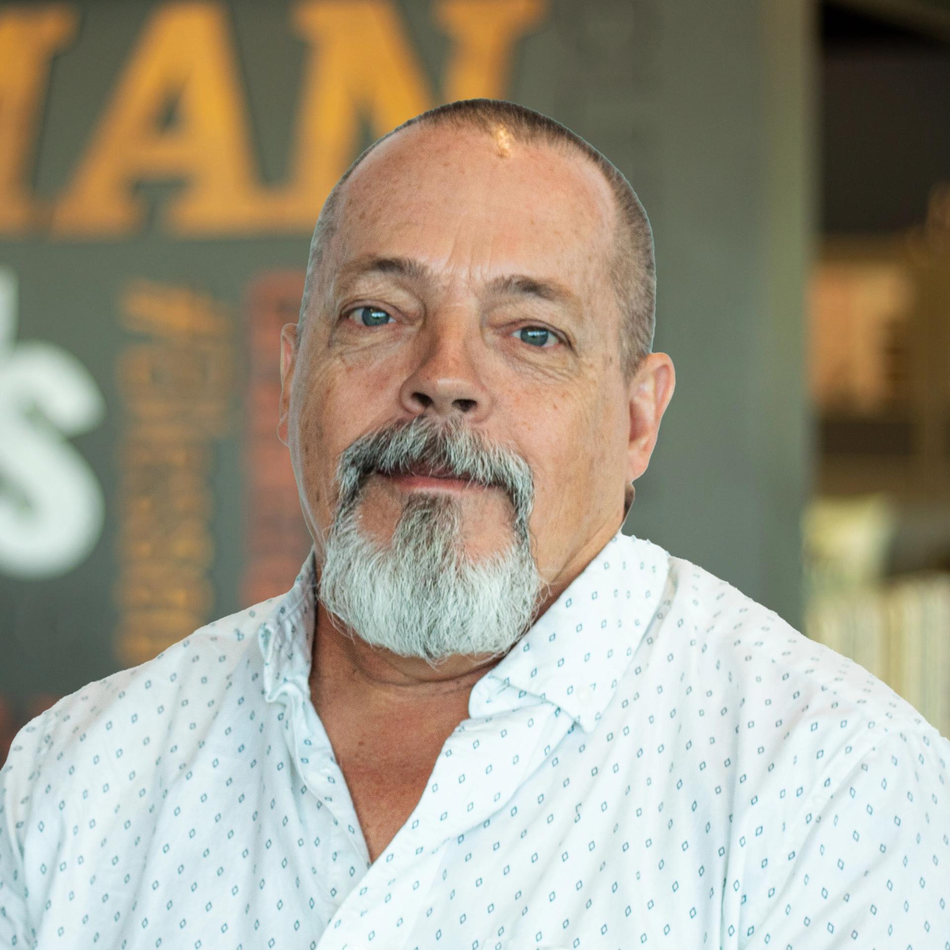 Bobby Hockenberry, wearing a white patterned button-down shirt, standing in front of a company-branded wall.