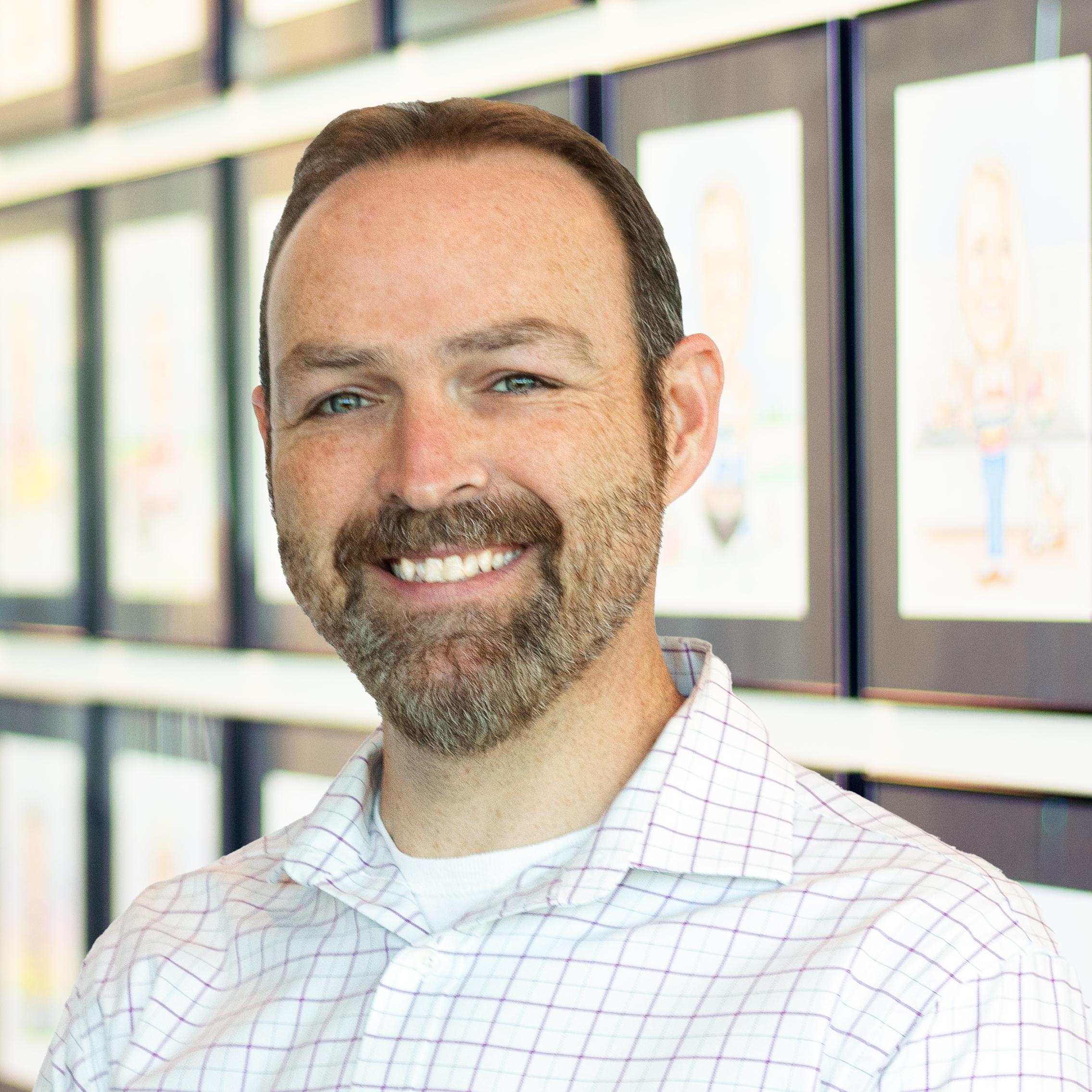 Patrick Everson wearing a smile and standing in front of a wall displaying framed caricatures.