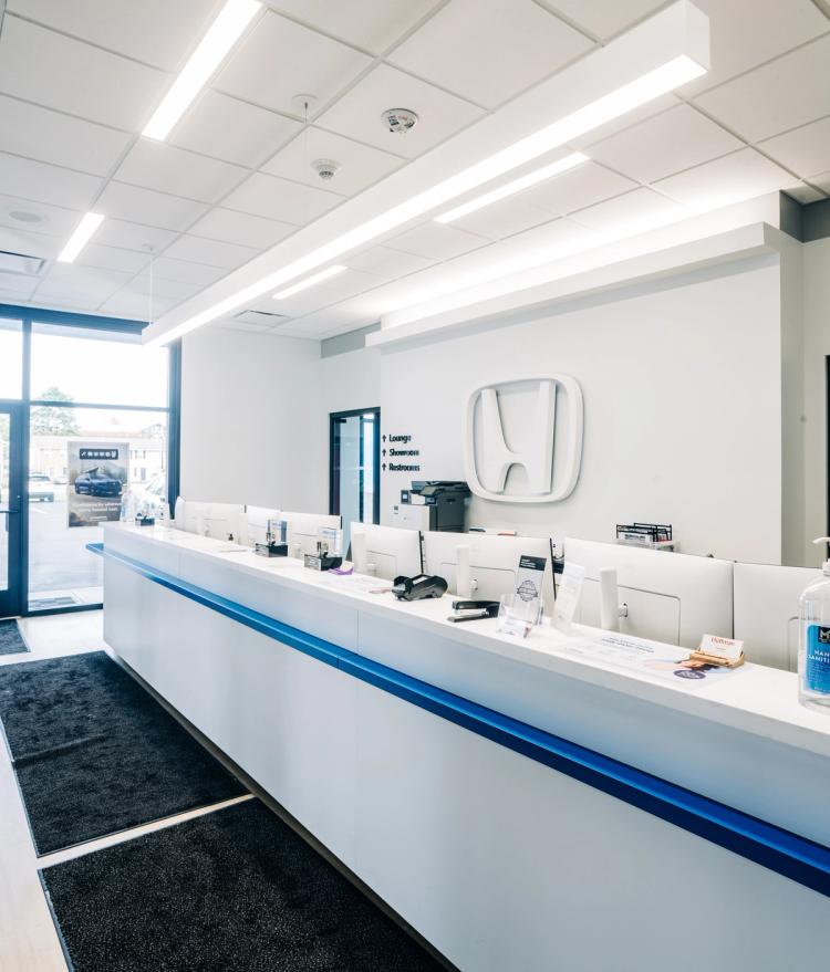 Completed Honda service reception area with a long white customer counter, blue accent detailing and a large illuminated Honda logo.